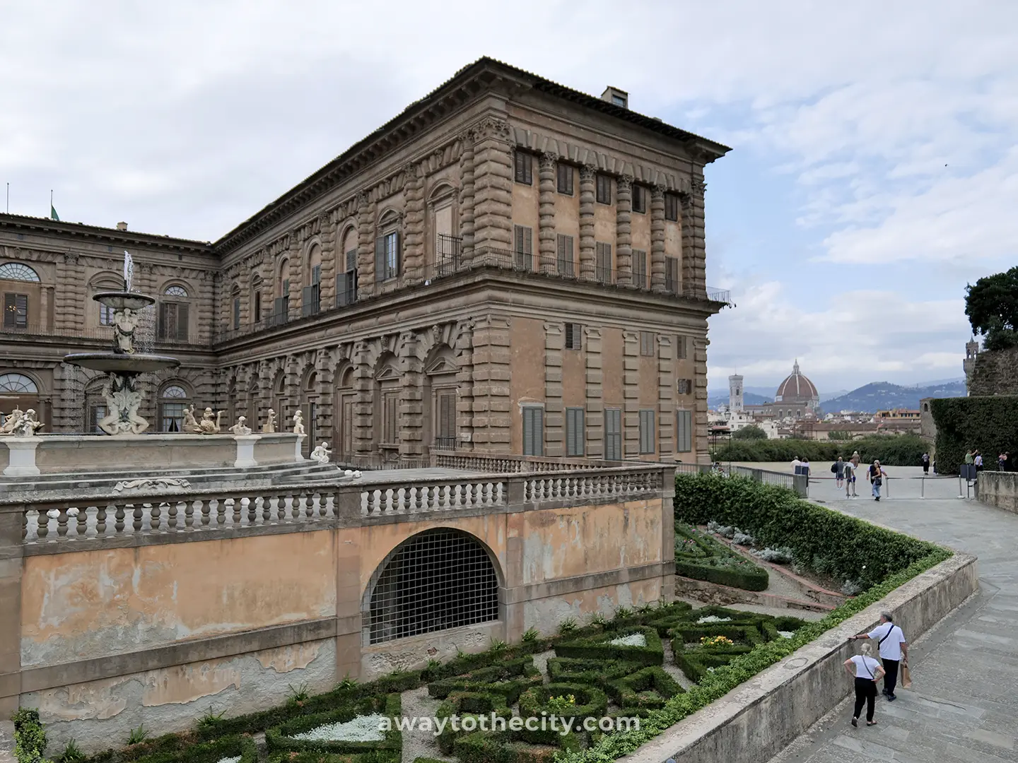 The grand facade of Pitti Palace overlooks the meticulously arranged Boboli Gardens, with Florence's Duomo visible in the distance, a stunning view on a 2-day Florence itinerary.