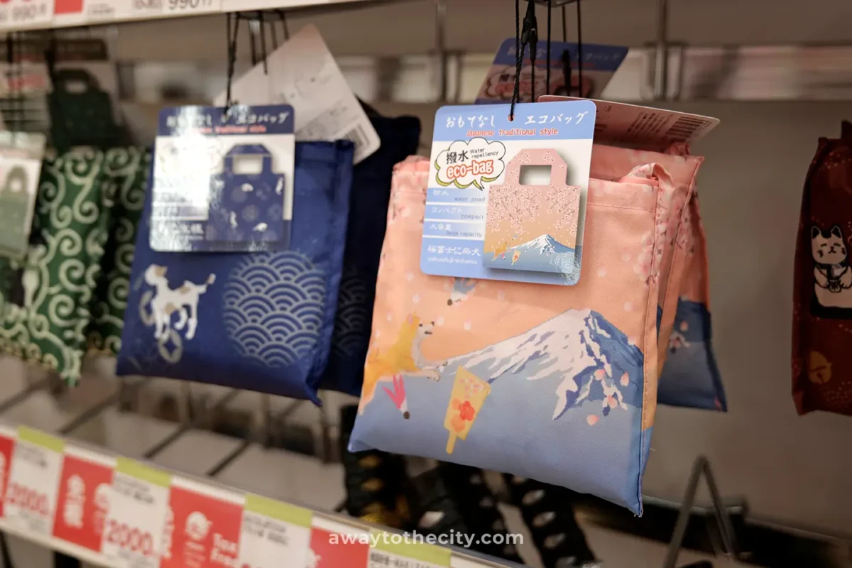 Reusable shopping bags with Japanese designs, including Mount Fuji and cherry blossoms, hang on display as eco-friendly souvenirs.