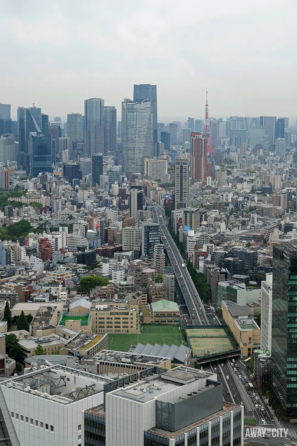 Dense Tokyo skyline with straight highway cutting through buildings and Tokyo Tower rising red among modern skyscrapers.