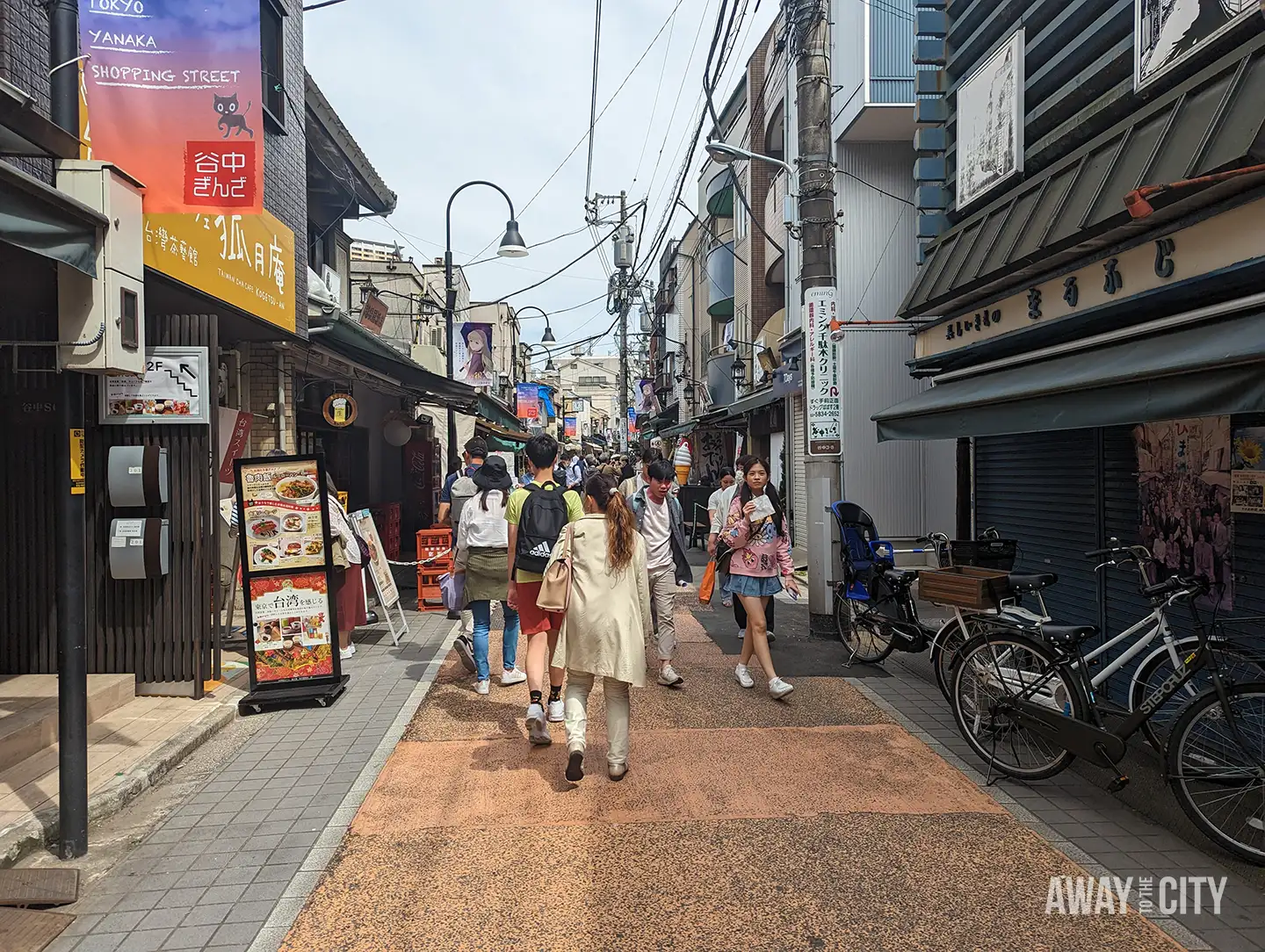 Busy pedestrian lane in Yanaka with small shops and signs including banner reading Tokyo Yanaka Shopping Street above narrow street.