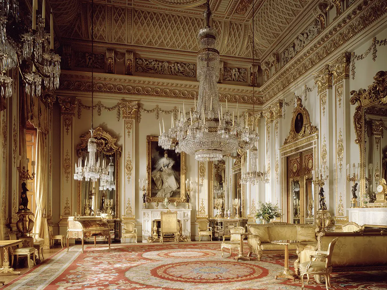 The White Drawing Room in Buckingham Palace, filled with ornate gold decor, a grand chandelier, and a portrait of a queen.