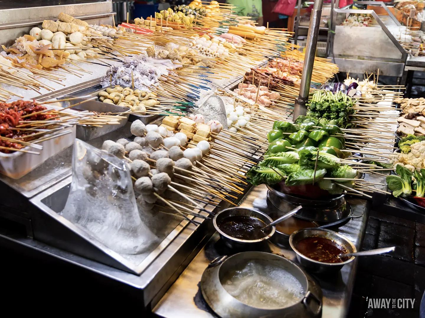 A street food stall in Jalan Alor, Kuala Lumpur, displays a wide array of skewered meats, vegetables, and seafood on ice.