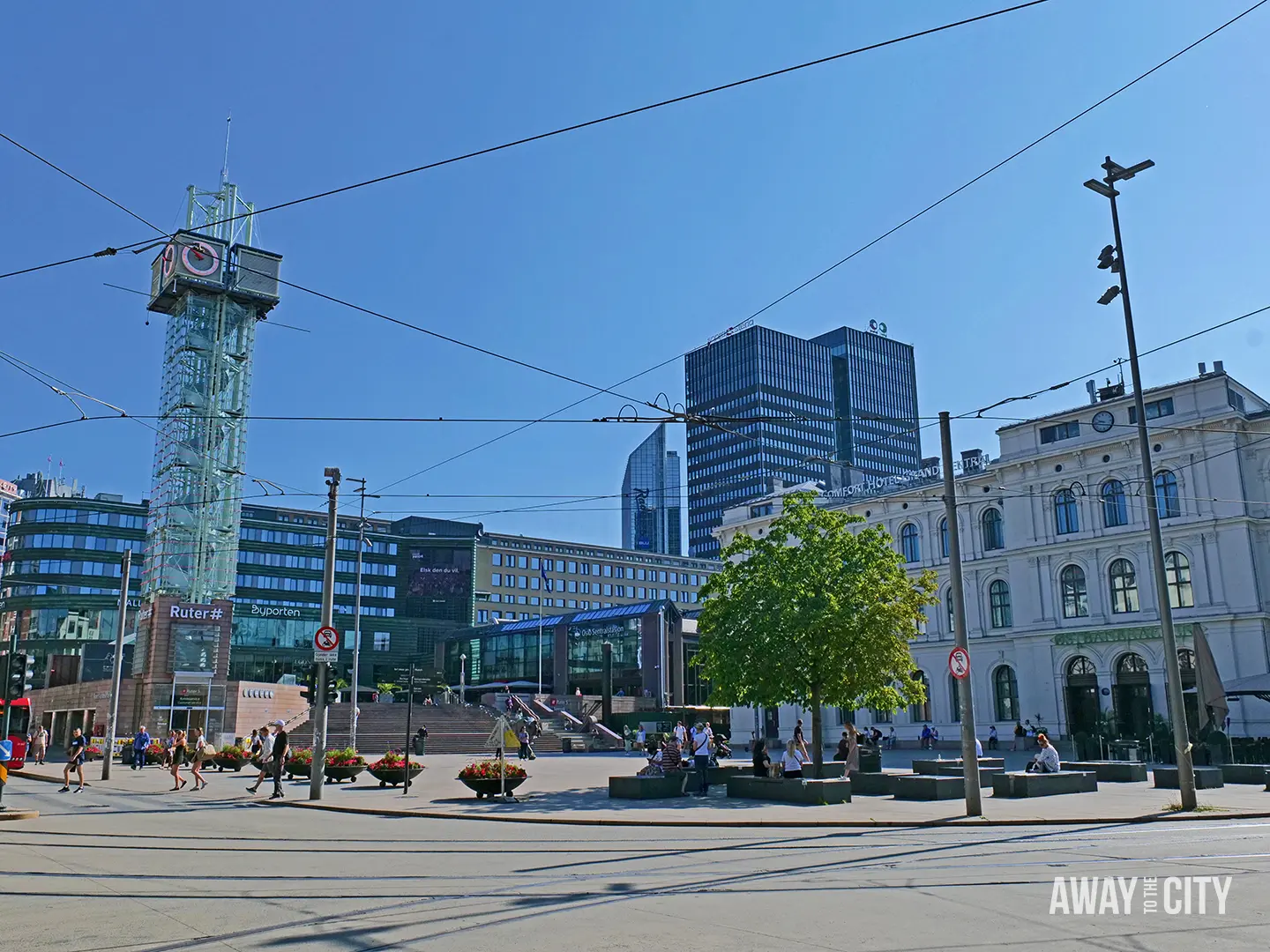 Oslo city square with tram wires, clock tower, pedestrians and modern buildings around Ruter# and Byporten near the central station.