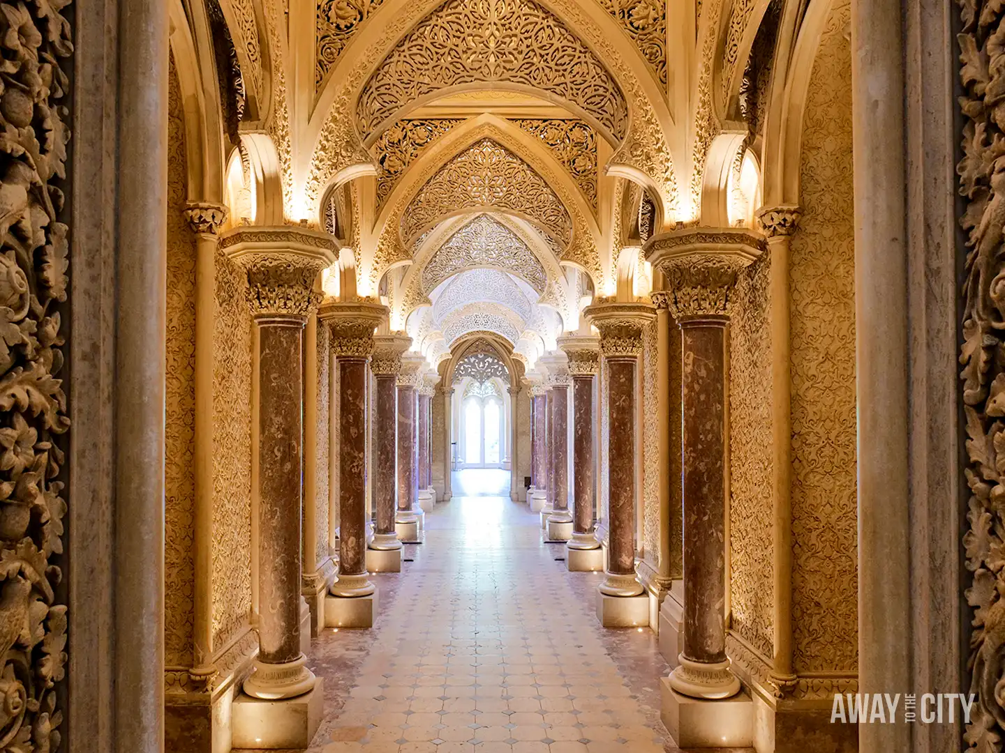Ornate hallway inside Monserrate Palace in Sintra, featuring richly decorated arches, carved details and illuminated columns.