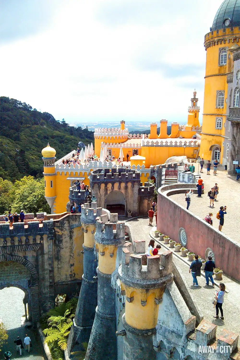 Visitors explore the colourful terraces and battlements of Pena Palace in Sintra, overlooking the surrounding hills.