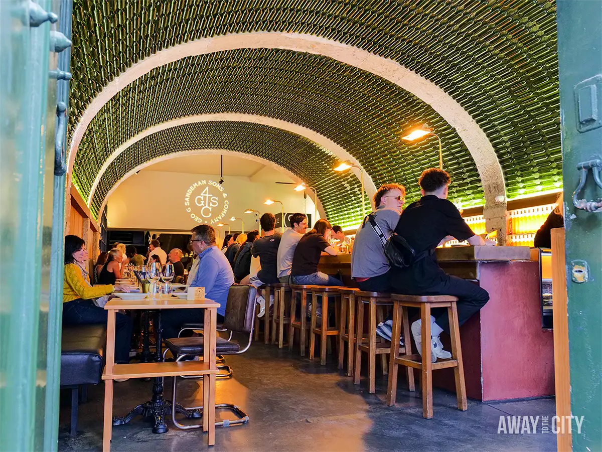 Customers at By The Wine in Lisbon’s Chiado district, beneath a vaulted ceiling covered with thousands of bottles.