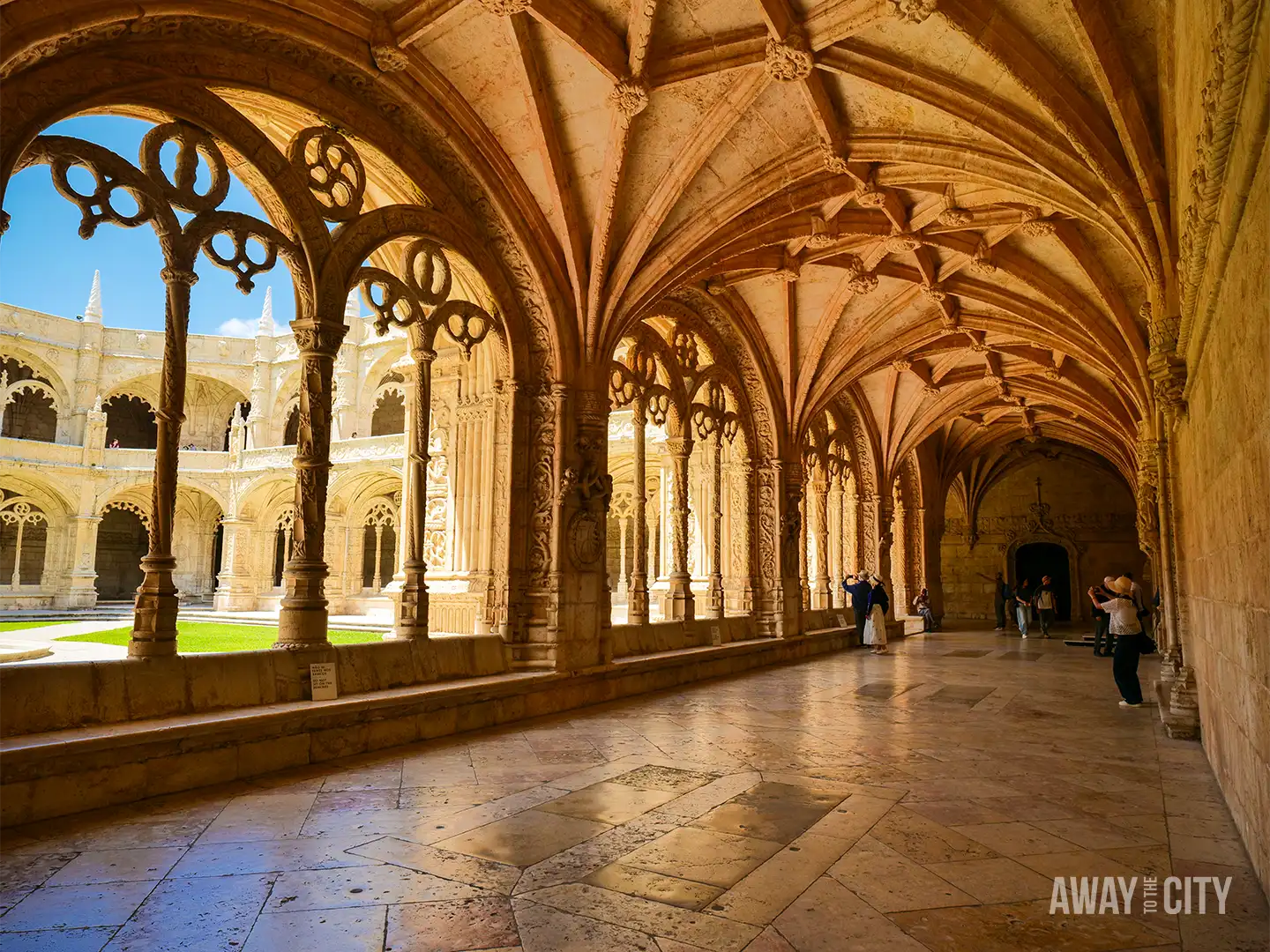Intricately carved cloister corridor inside Jerónimos Monastery in Belém, Lisbon, featuring vaulted ceilings and decorative stone columns.