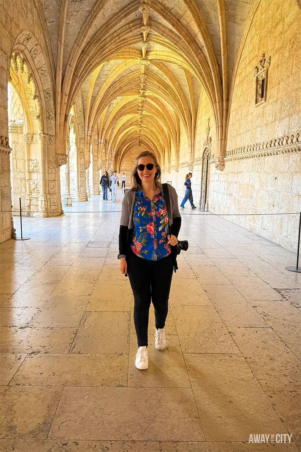 A person walking beneath vaulted stone arches inside Jerónimos Monastery in Belém, Lisbon, showcasing ornate Manueline architecture.