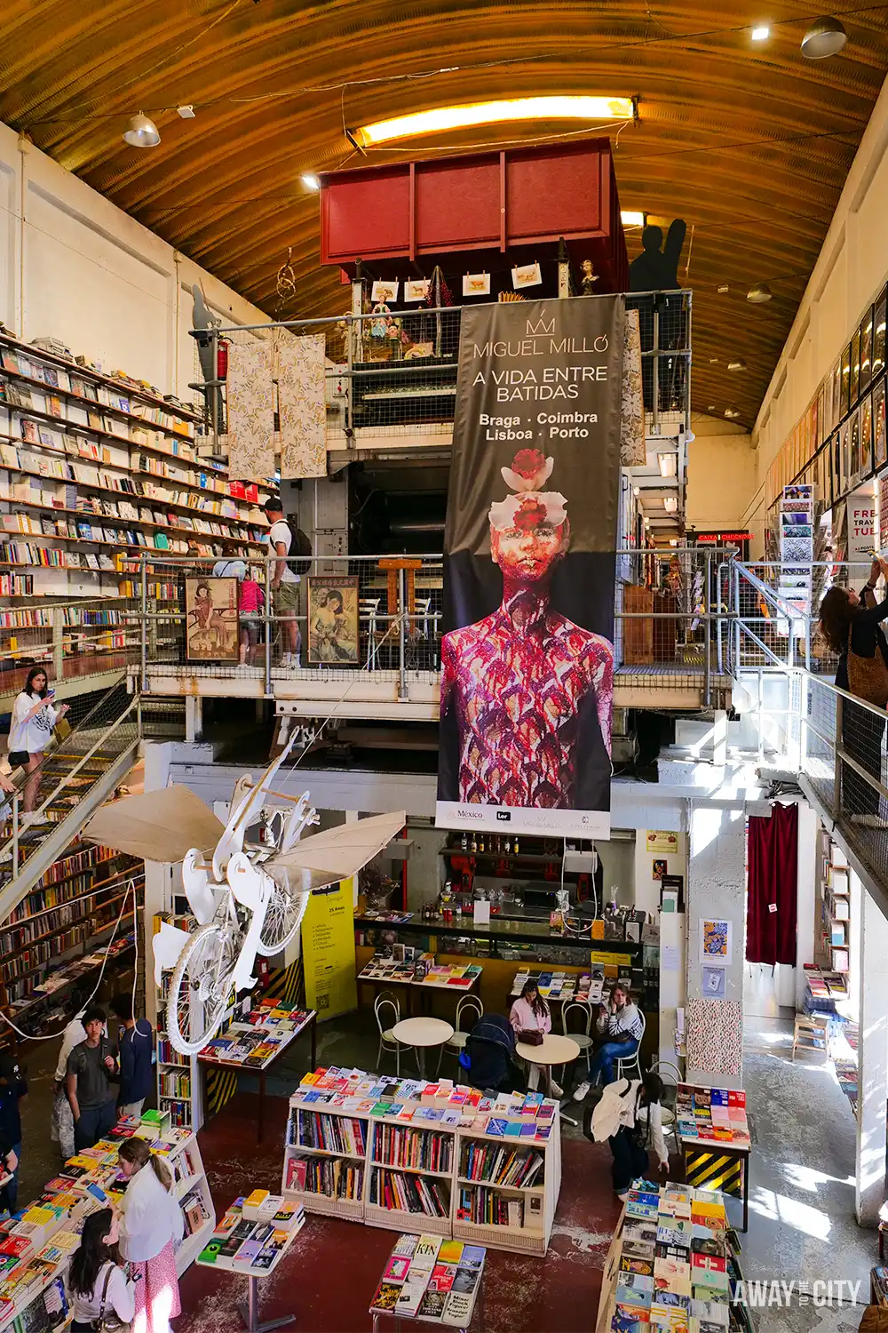 Interior of Livraria Ler Devagar at LX Factory in Lisbon, featuring towering bookshelves, reading areas and suspended artwork.