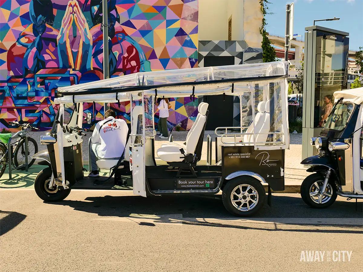 Tuk-tuk parked outside LX Factory in Lisbon, with the colourful Listen to Your Soul mural visible in the background.