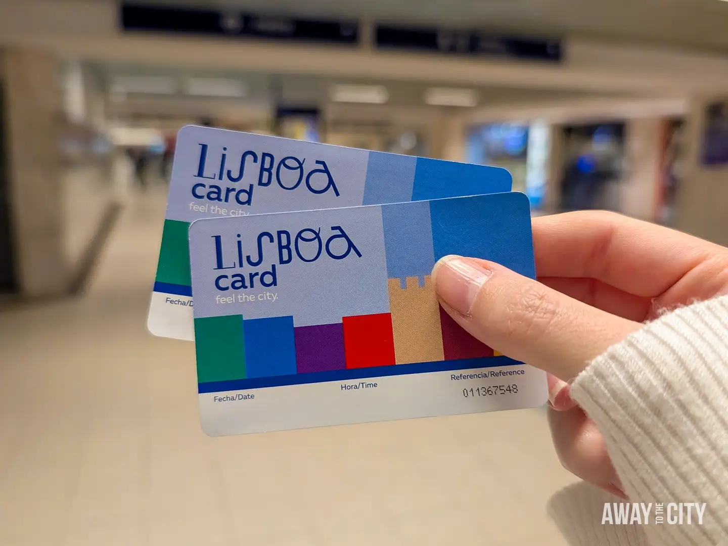 Hand holding two Lisboa Cards inside a metro station, used for public transport and attraction access in Lisbon.