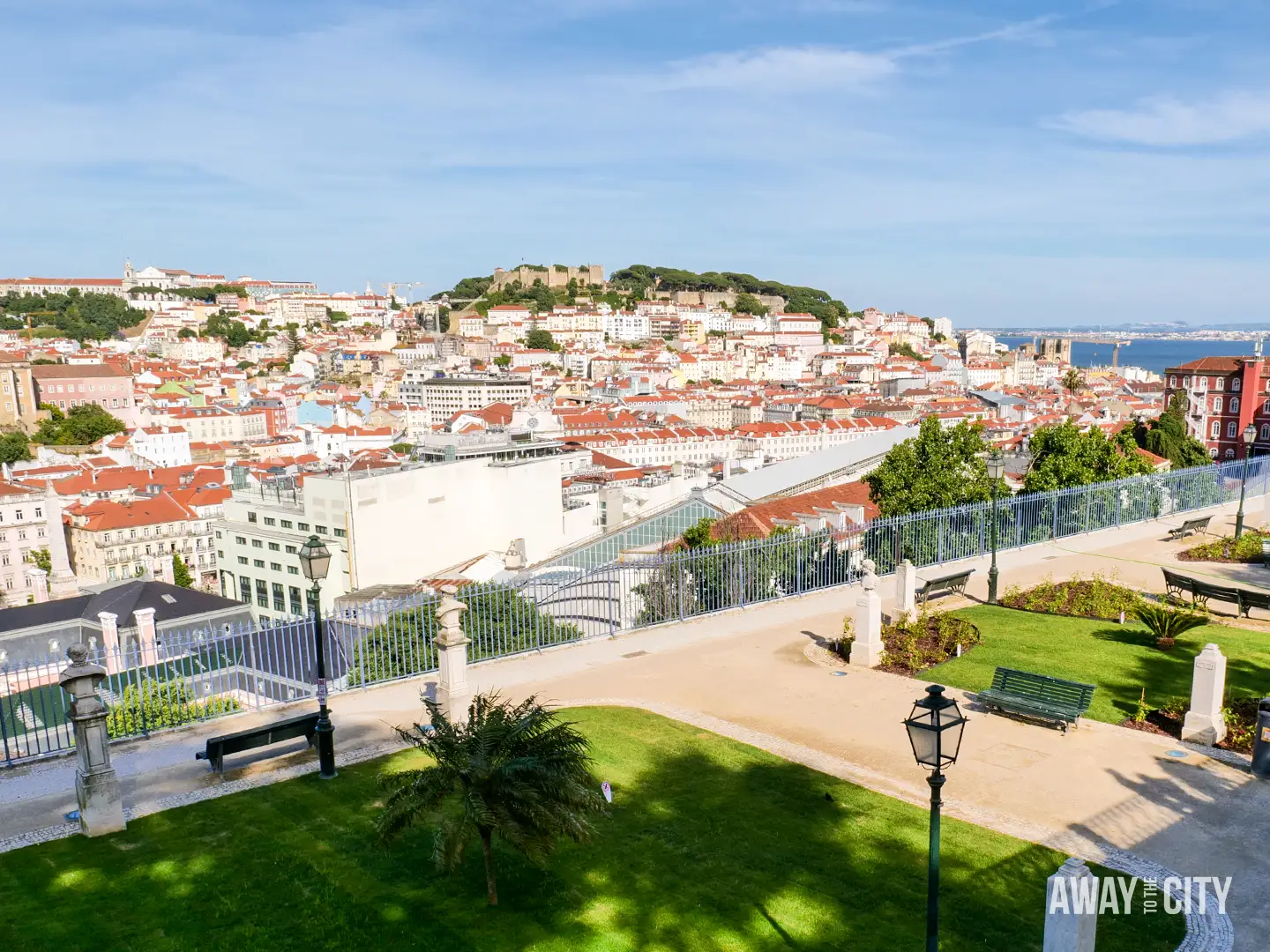 Panoramic view over Lisbon from Miradouro de São Pedro de Alcântara, with gardens, rooftops and São Jorge Castle visible.