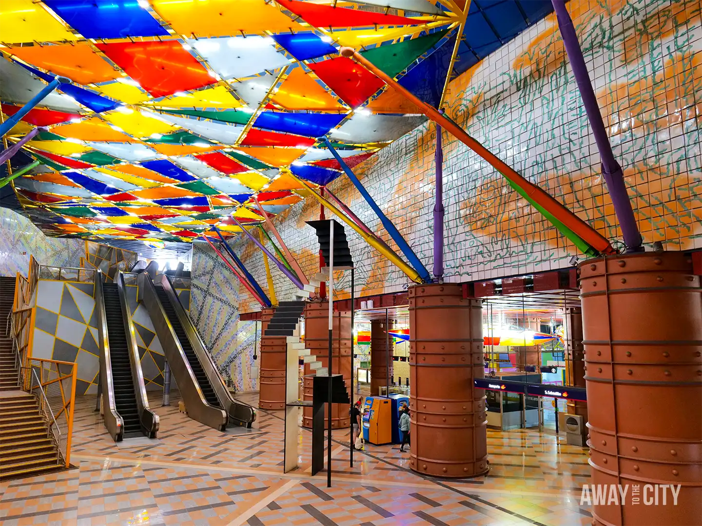 Colourful interior of Olaias Metro Station in Lisbon, featuring geometric ceiling panels, escalators and distinctive industrial-style columns.