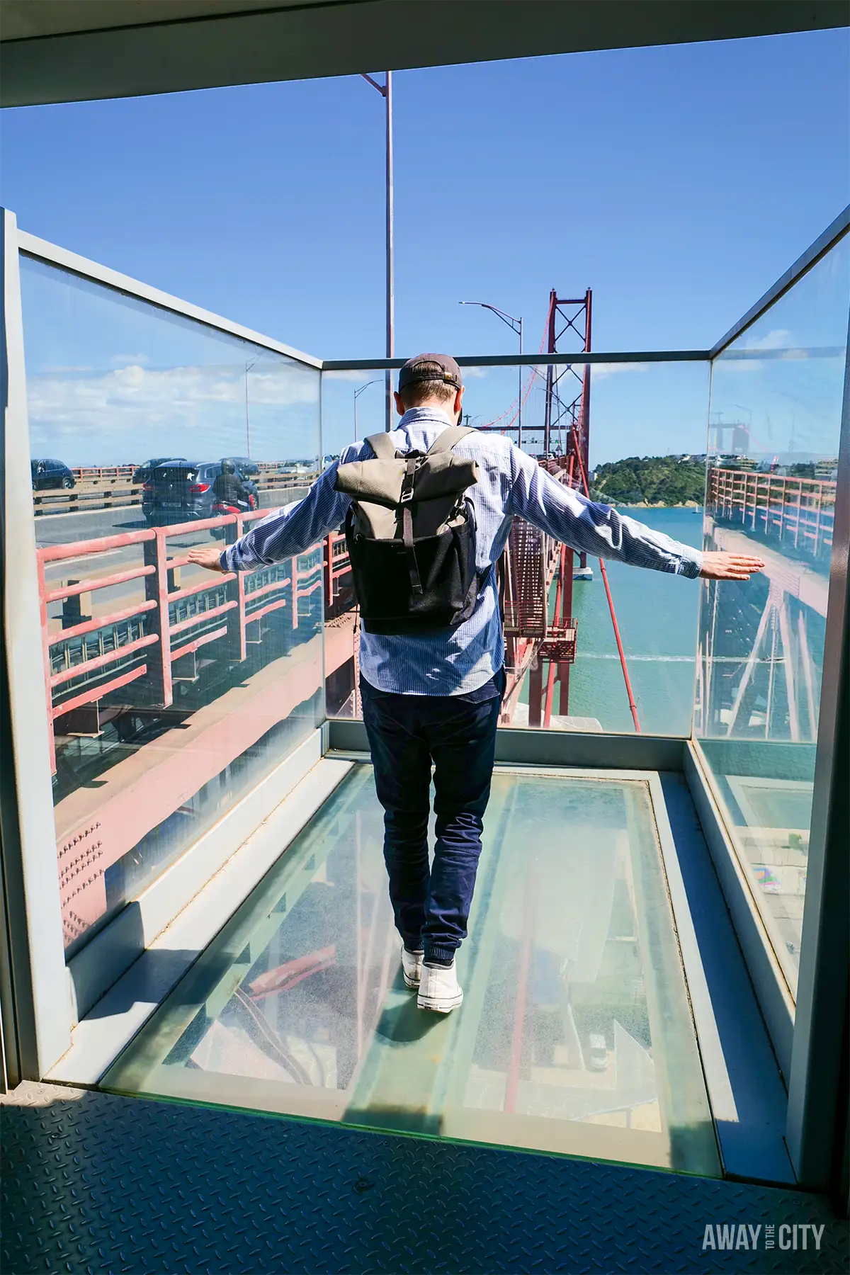 Visitor walks across a glass viewing platform at the Pilar 7 Bridge Experience in Lisbon, overlooking the Tagus River.