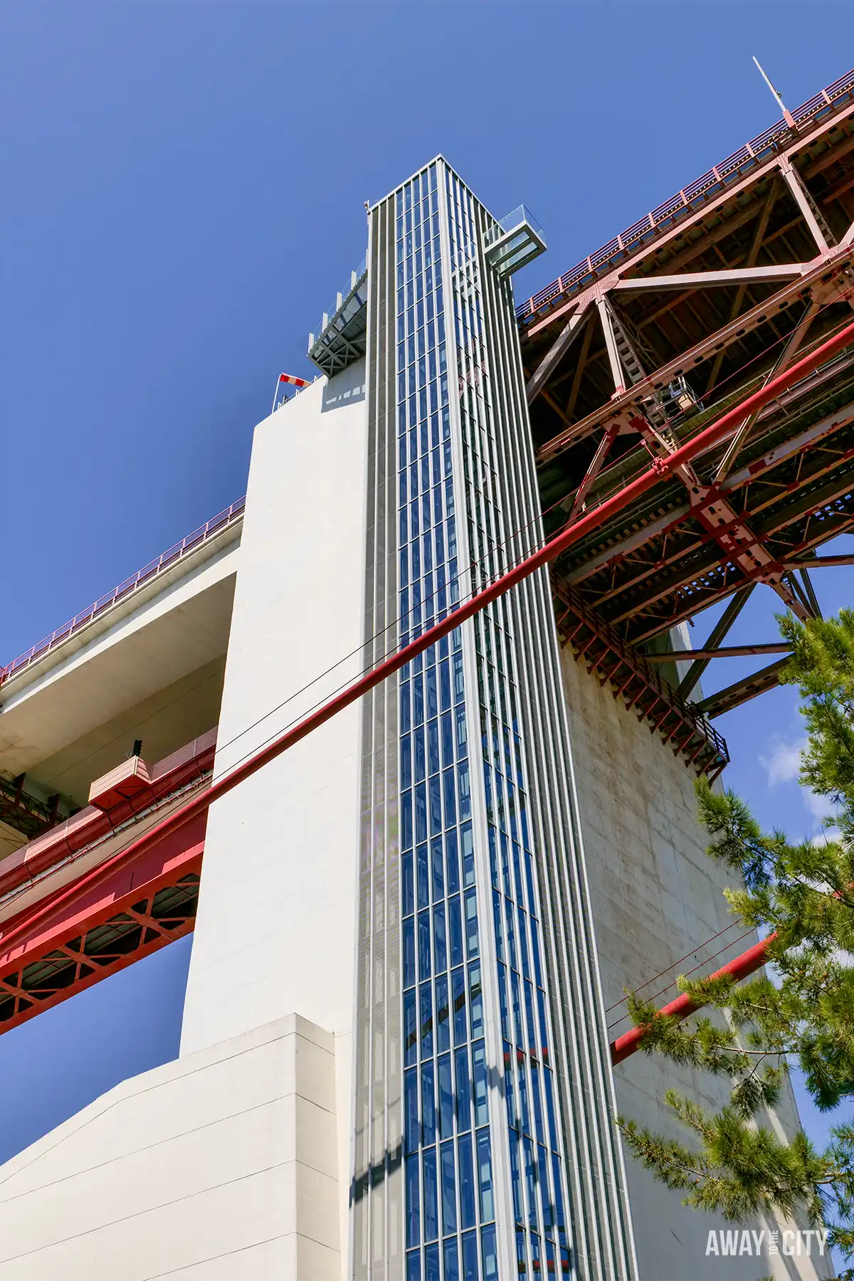 Looking up at the lift tower and red steel structure of Lisbon’s 25 de Abril Bridge at Pilar 7.
