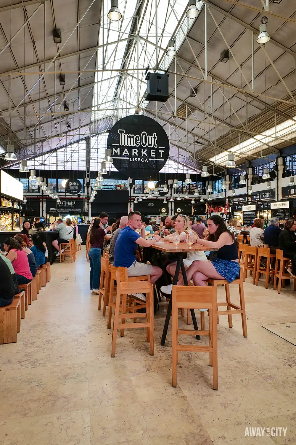 Visitors dine at communal tables beneath the TimeOut Market Lisboa sign inside Lisbon’s bustling indoor food hall.