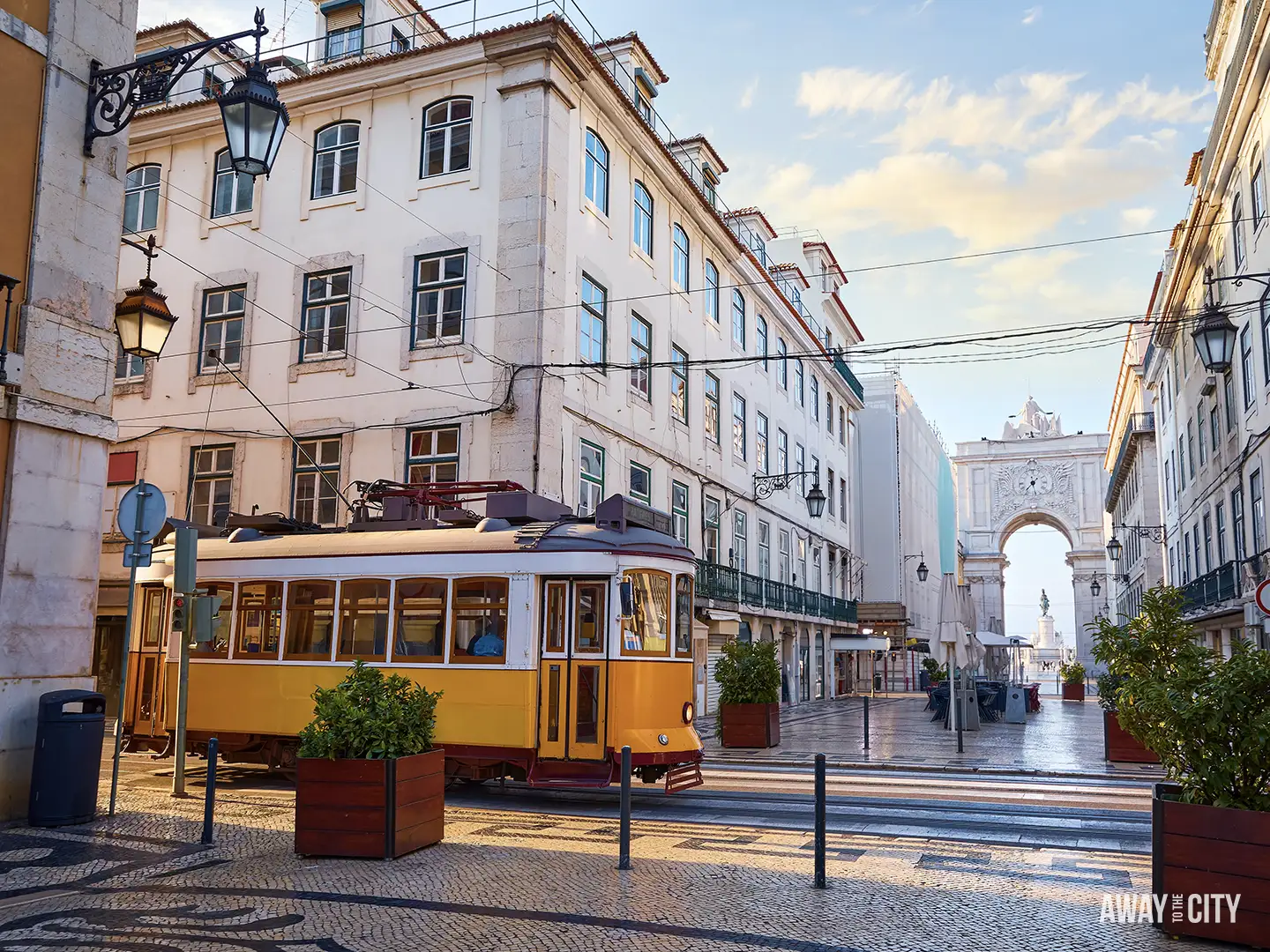 A classic bright yellow tram sits on a cobblestone street in Lisbon, with the white Arco da Rua Augusta visible in the background.