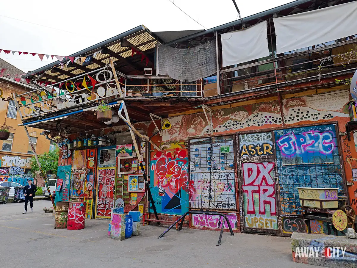 Colourful exterior of AKC Metelkova Mesto in Ljubljana with graffiti-covered walls, eclectic decorations, and layered balconies filled with artistic details.