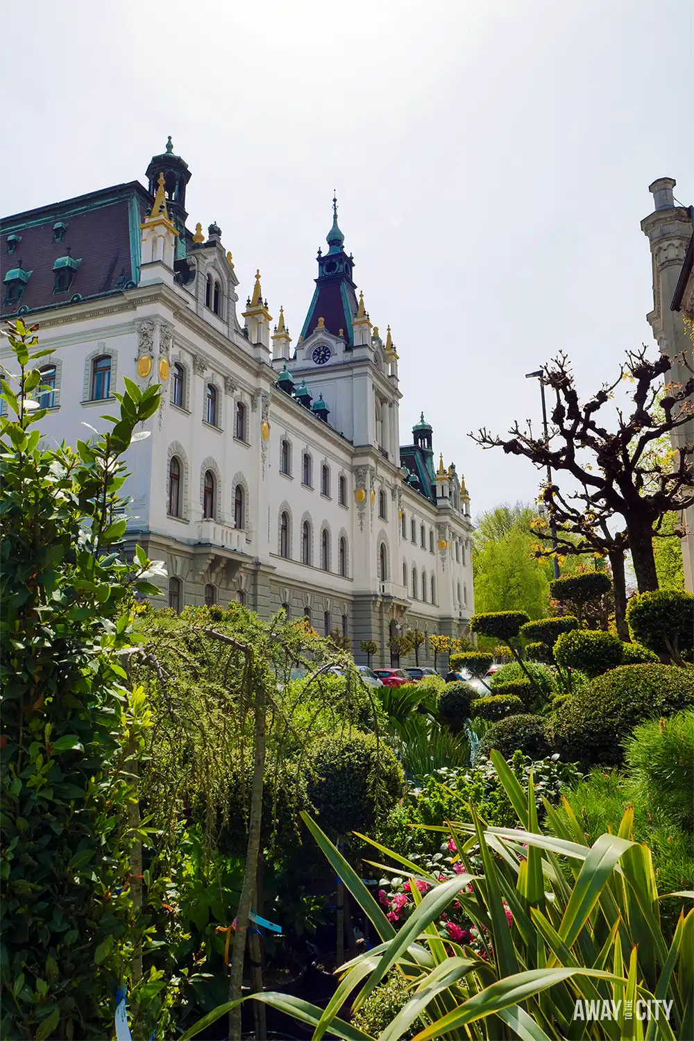Congress Square in Ljubljana with manicured gardens, trimmed trees, and view of University building under bright sky.