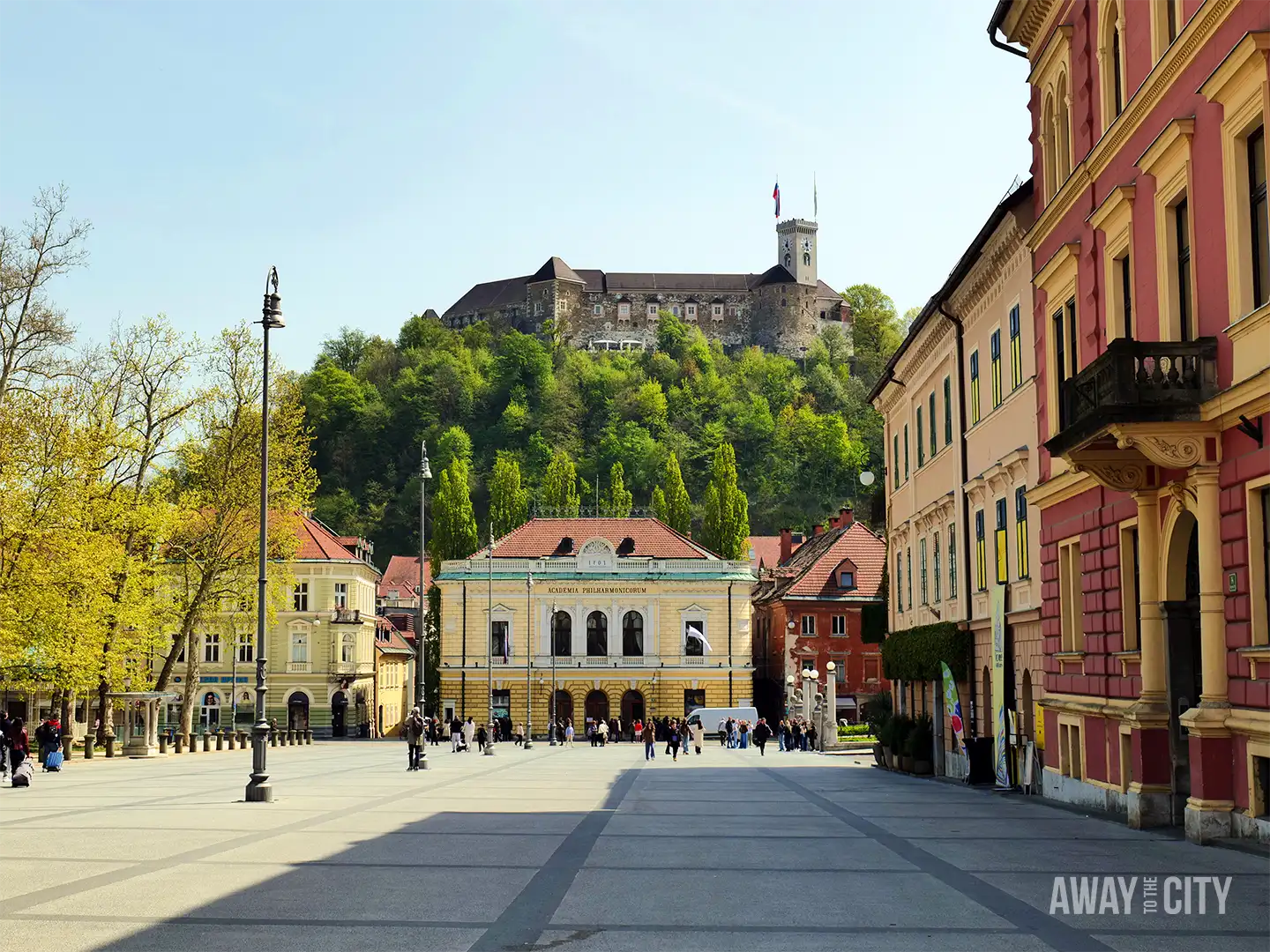 Congress Square in Ljubljana with Zvezda Park, Slovene Philharmonic building, and Ljubljana Castle on hill overlooking wide open plaza with pedestrians.