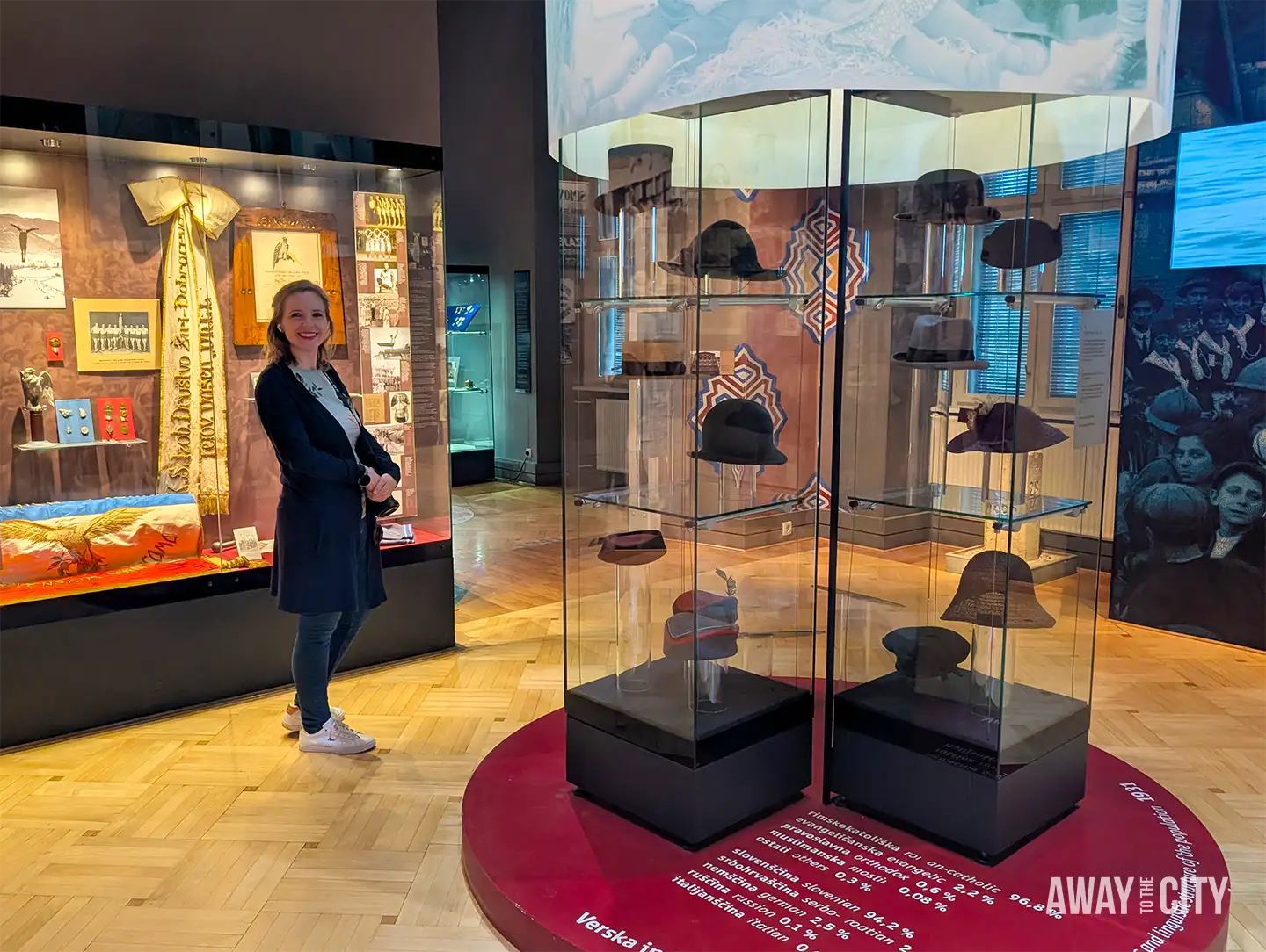 Interior of National Museum of Contemporary History with glass display of hats, historical exhibits, and visitor standing beside illuminated artefacts and information panels.