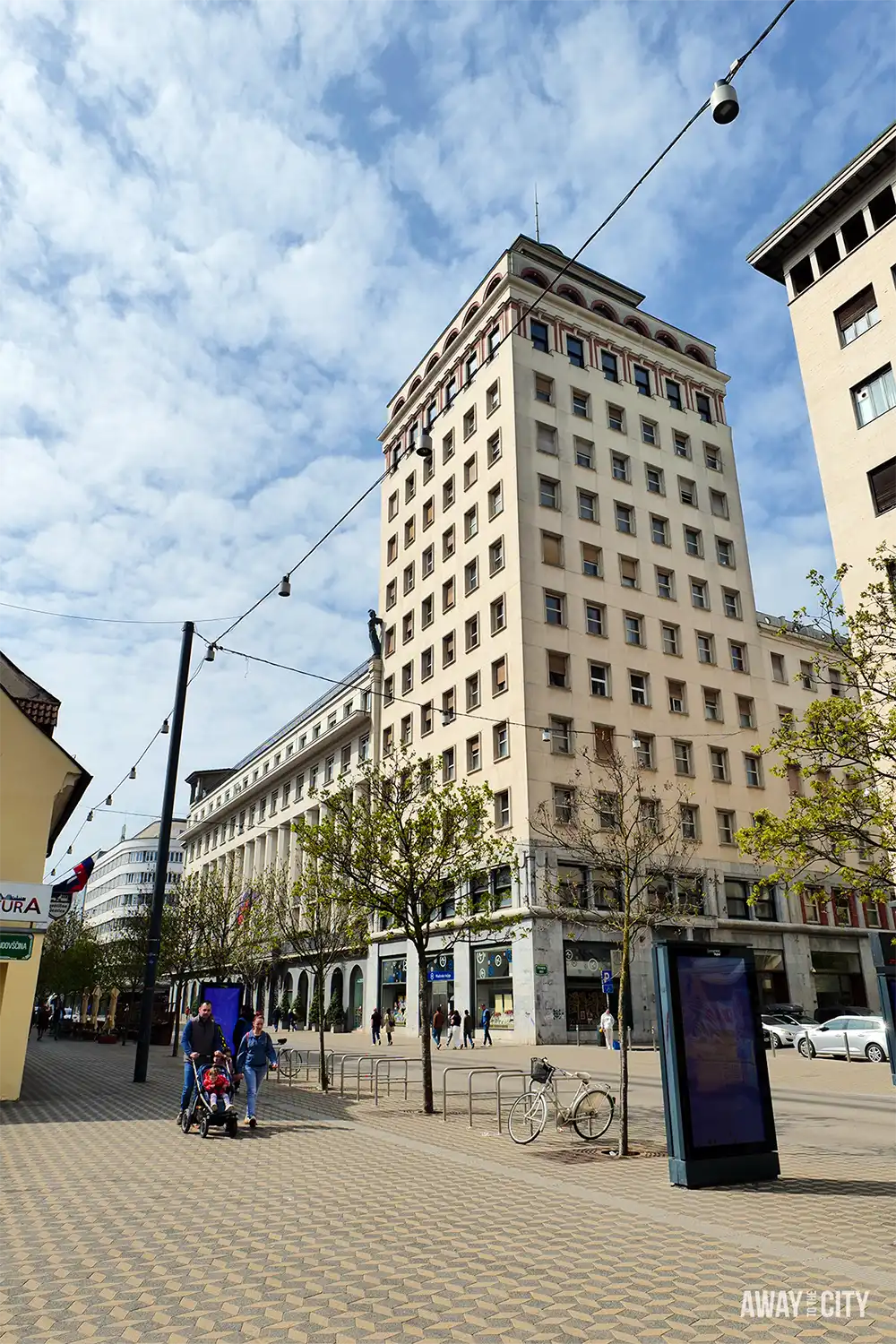 Street-level view near Nebotičnik Skyscraper with modernist building, pedestrians, and open square framed by surrounding city architecture.