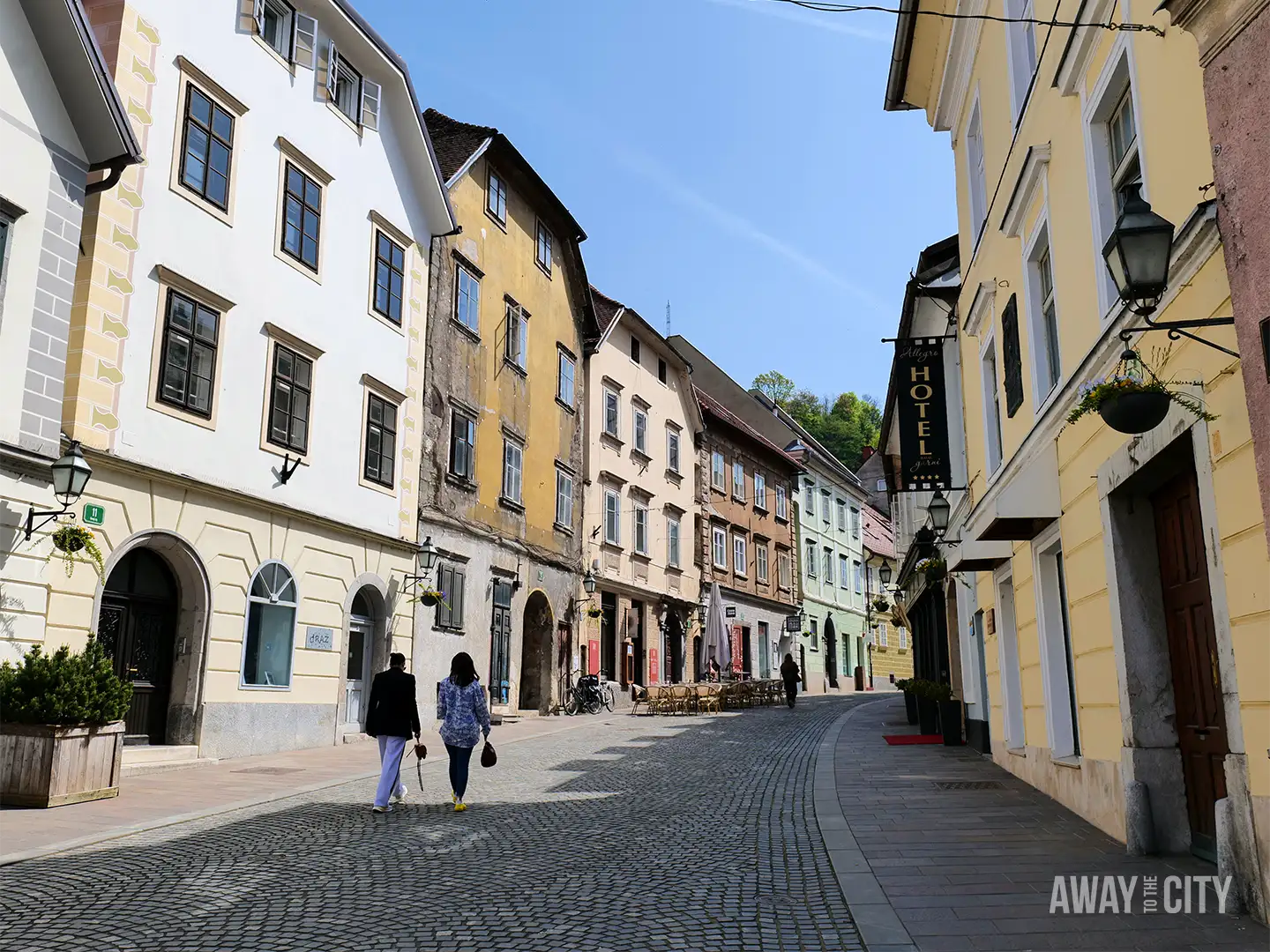 Mestni Trg in Ljubljana with cobbled square, pastel baroque buildings, café seating, and town hall tower rising beneath a clear blue sky.