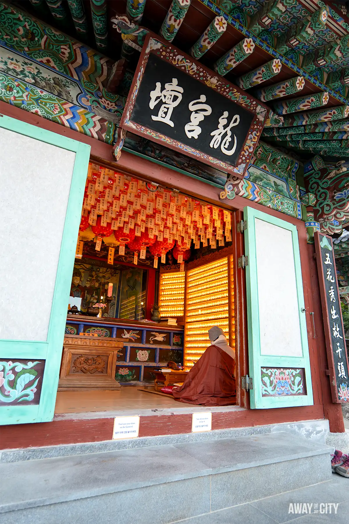 Monk seated inside colourful temple hall at Haedong Yonggungsa Temple in Busan, surrounded by glowing lanterns and illuminated prayer candles.