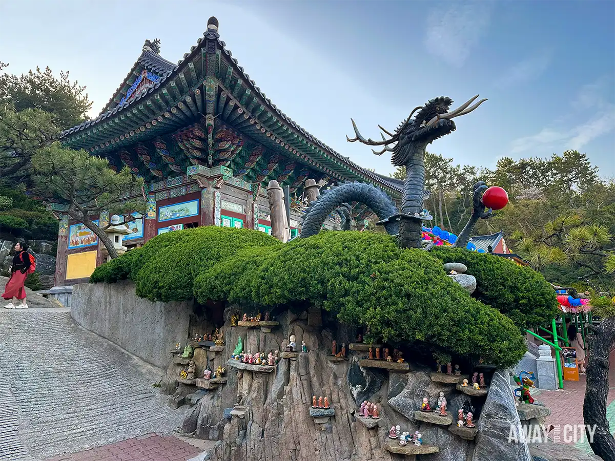 Dragon sculpture beside traditional temple pavilion at Haedong Yonggungsa Temple in Busan, with small statues arranged along the hillside.