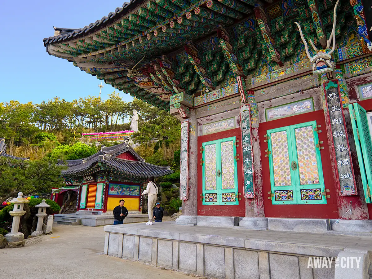Ornately decorated main buddha hall building at Haedong Yonggungsa Temple in Busan, featuring colourful wooden details and visitors exploring the seaside complex.
