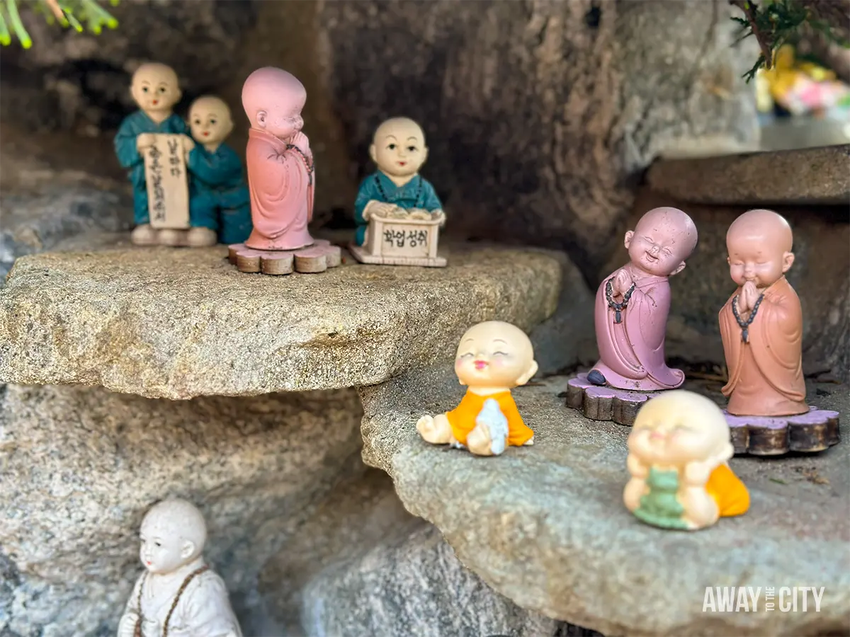 Small monk figurines placed on rocky ledges at Haedong Yonggungsa Temple in Busan, featuring colourful robes and prayer poses.