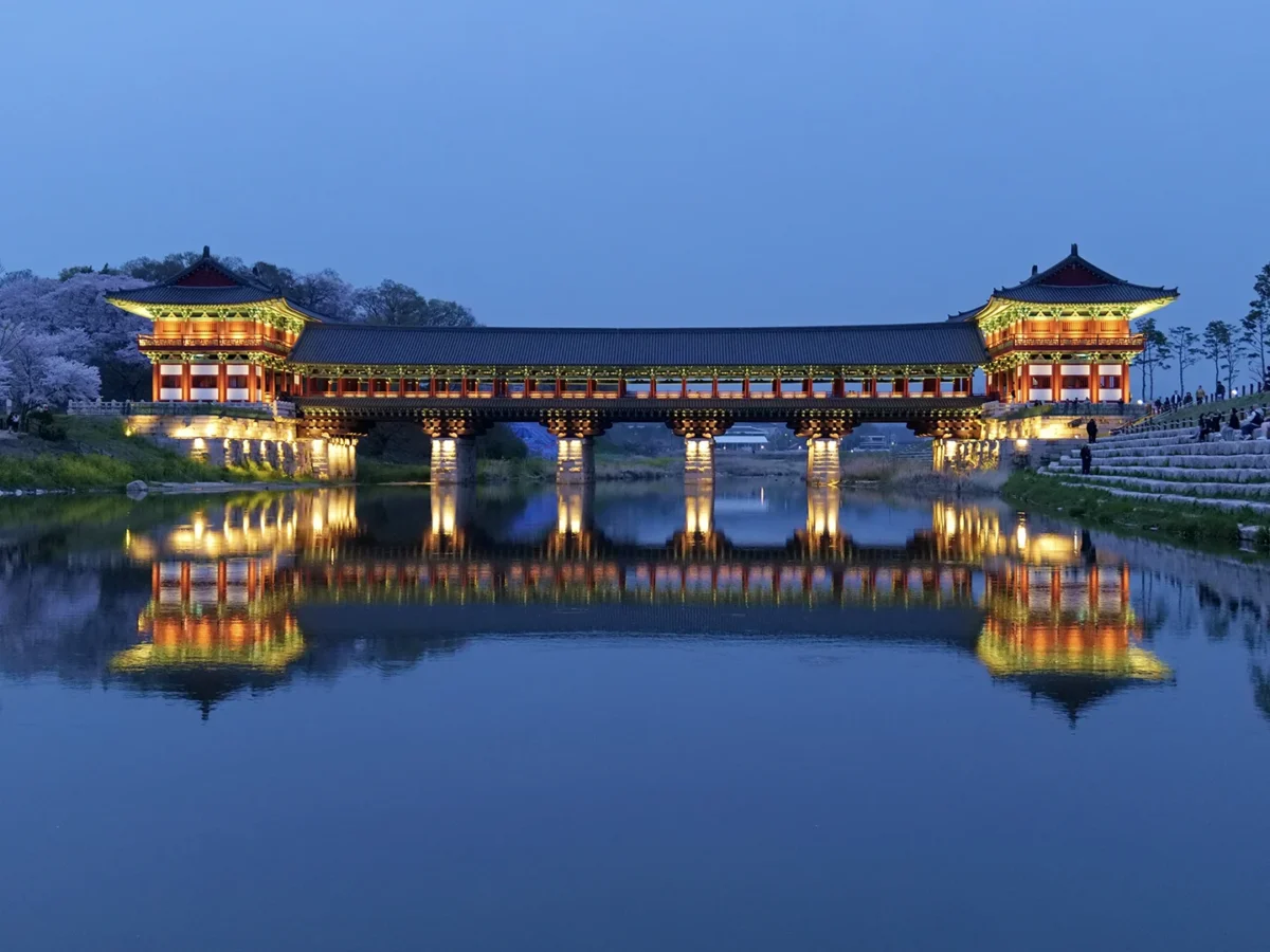 Gyeongju's illuminated Woljeong Bridge, a traditional Korean structure, is beautifully reflected in the still water at twilight.