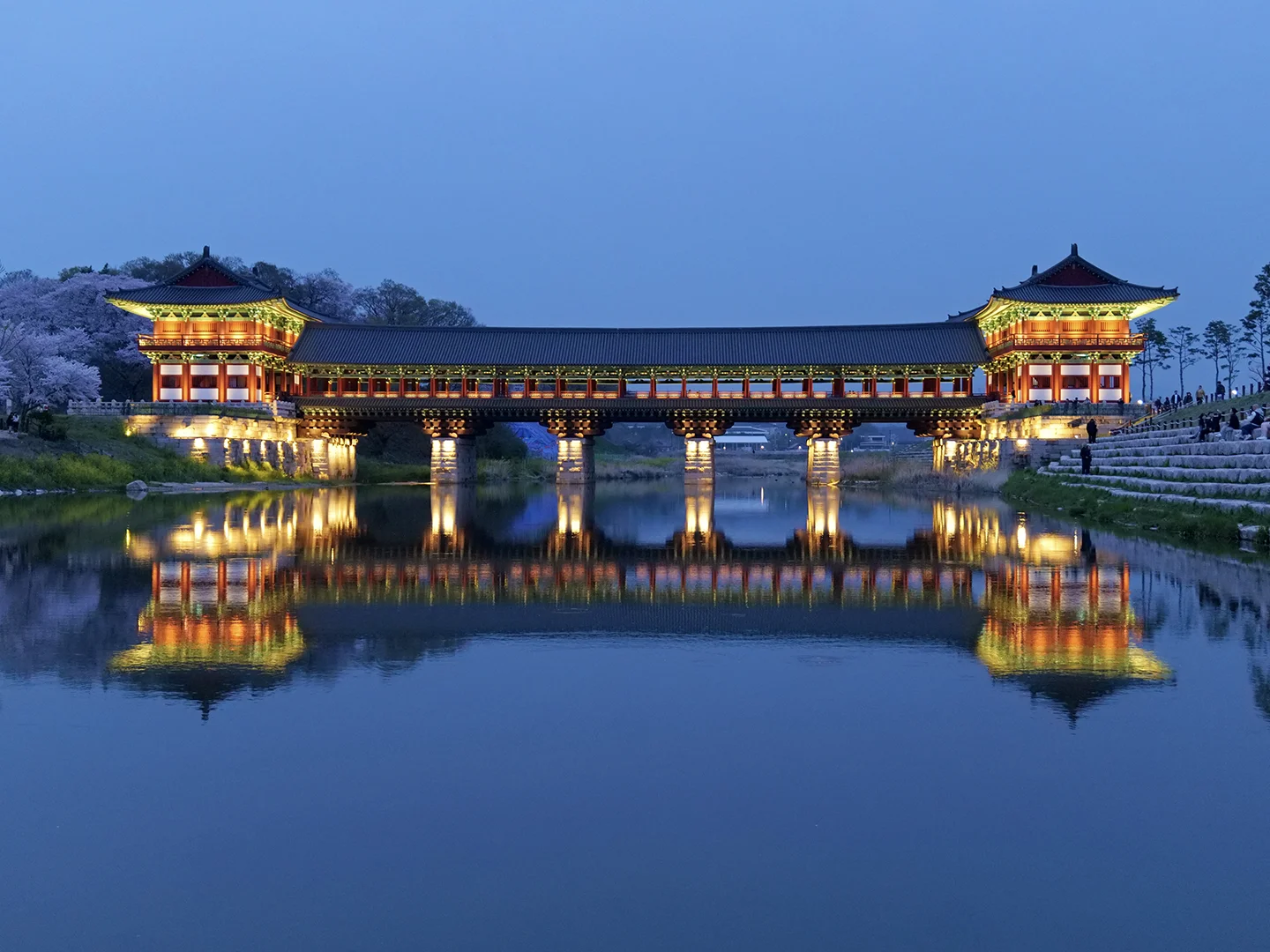 Gyeongju's illuminated Woljeong Bridge, a traditional Korean structure, is beautifully reflected in the still water at twilight.