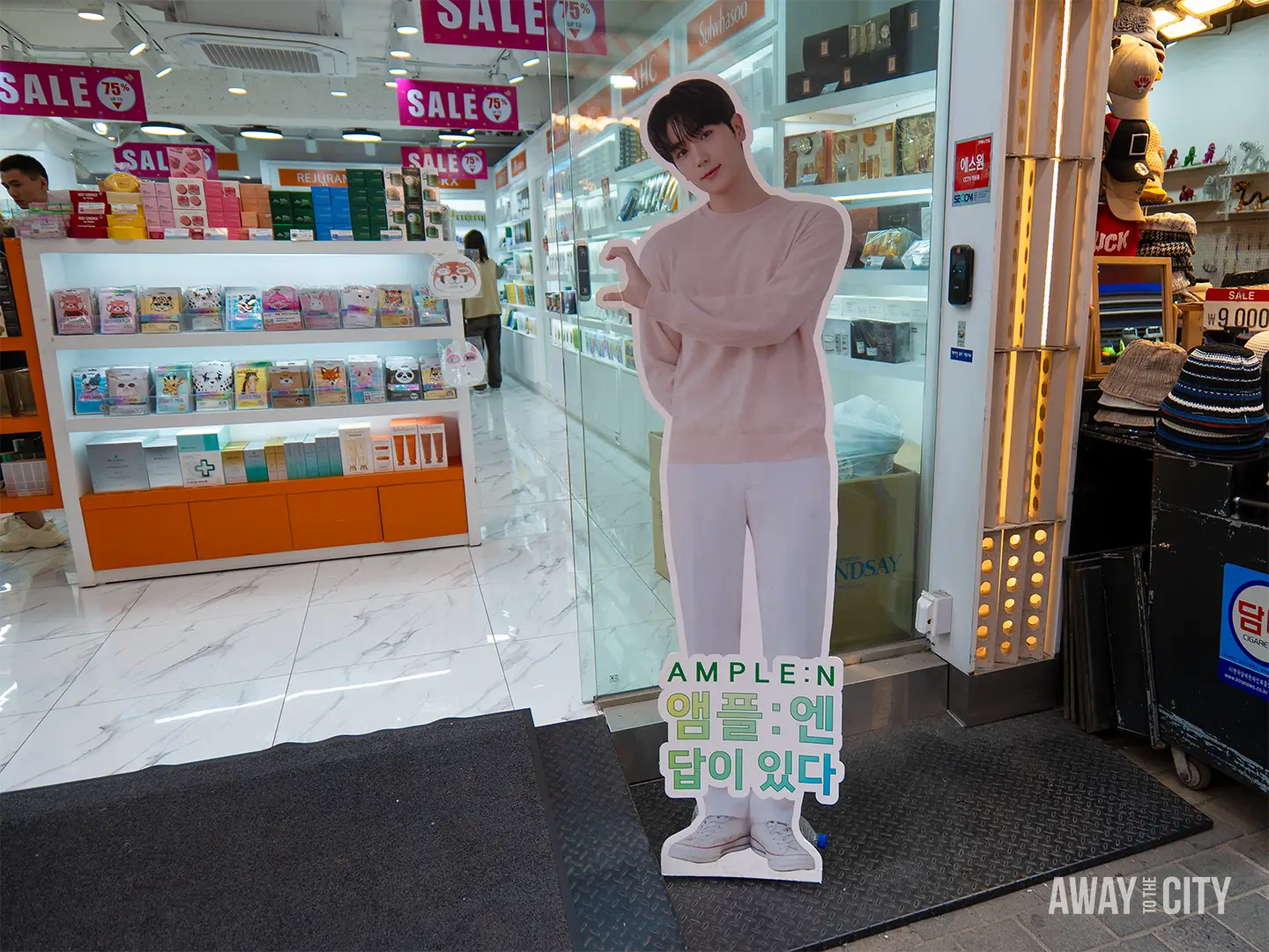 A cardboard standee promoting AMPLE:N Korean skincare outside a drugstore in Myeongdong.