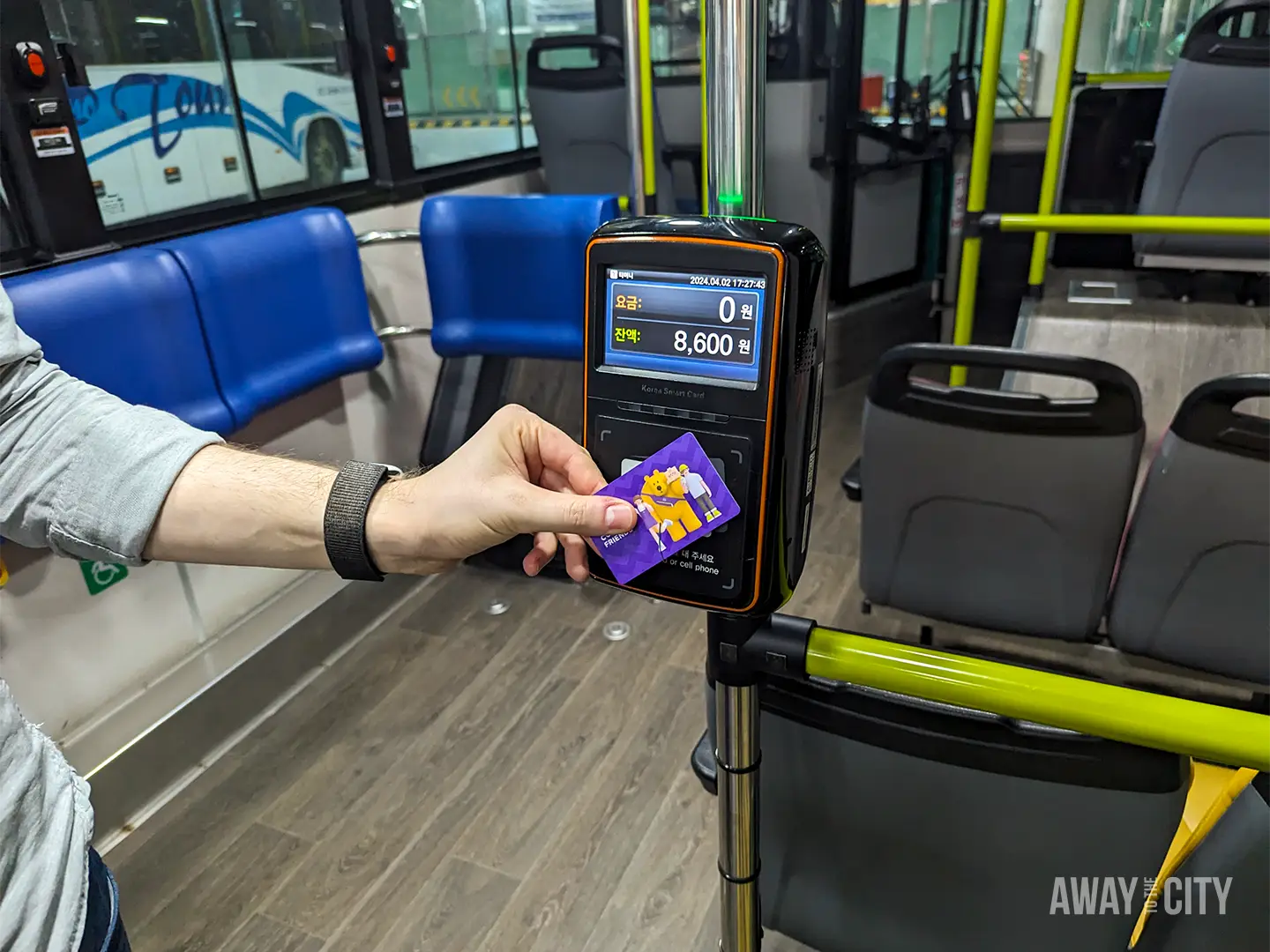 Hand holding a transport card against a bus fare reader, with remaining balance displayed on the onboard screen.