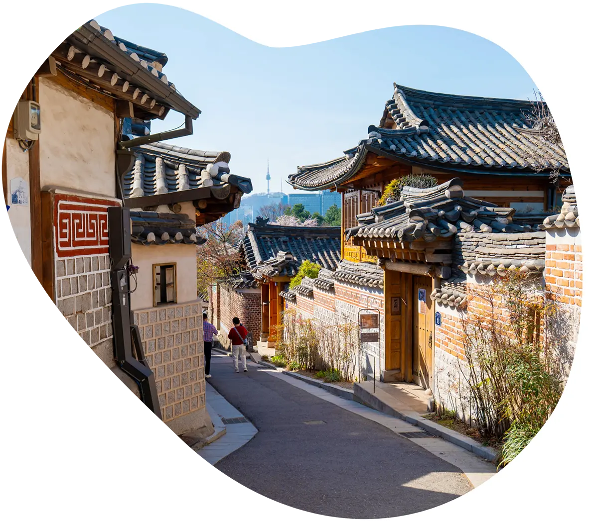 Traditional hanok houses lining a narrow street in Bukchon Hanok Village, with N Seoul Tower visible above Seoul skyline in distance.