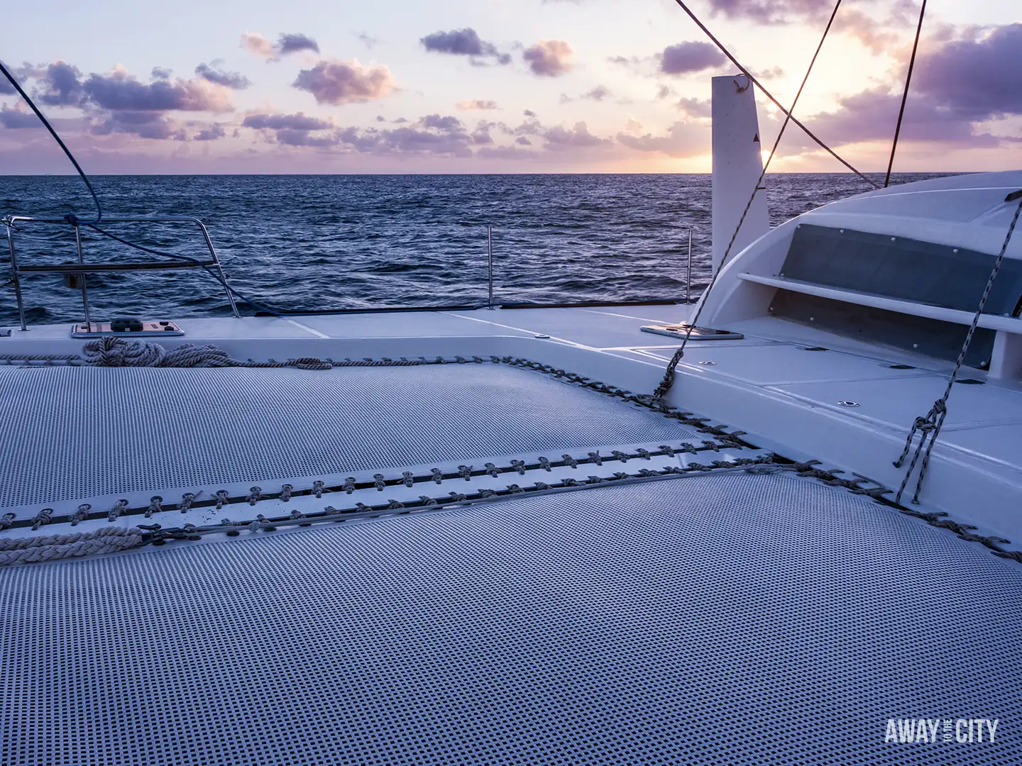 A sunset view over the sea from the deck and netting of a catamaran cruise.
