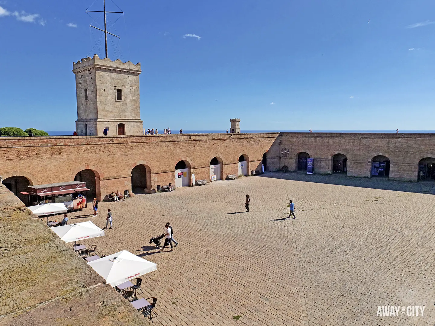 The sunlit central parade ground of Montjuïc Castle in Barcelona, showing the red brick walls and the tall stone keep.