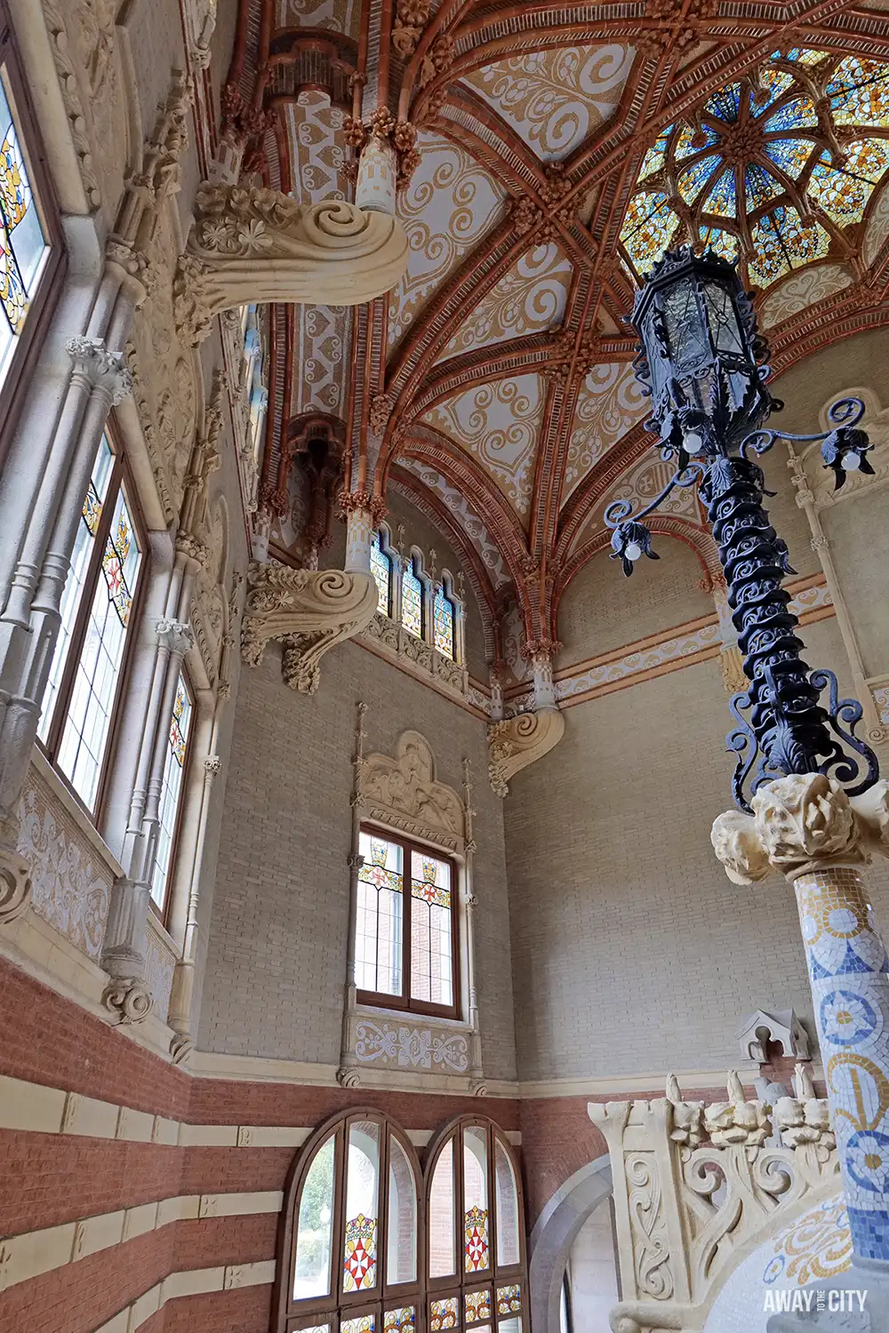 The grand interior of the Administration Pavilion at Sant Pau hospital, showing a vaulted ceiling, stained glass, and an ornate lamp.
