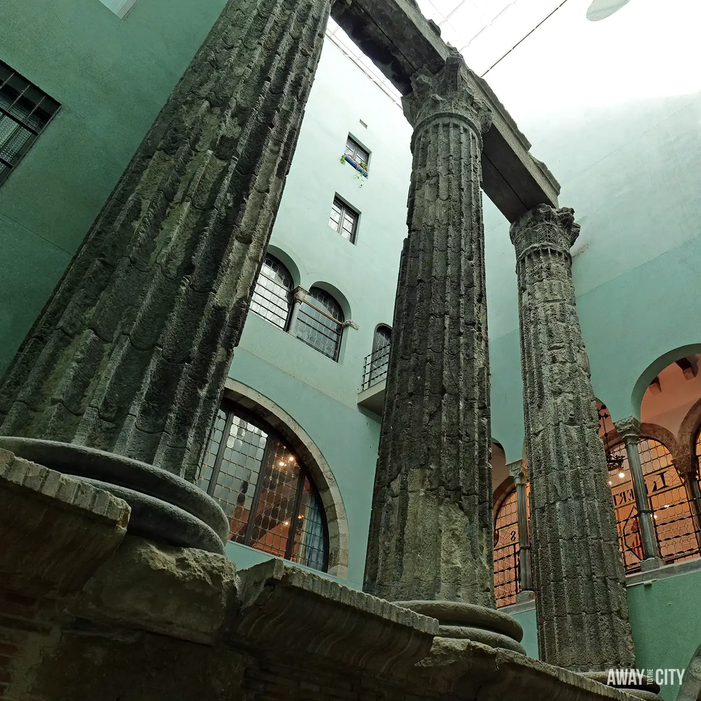 An upwards view of three massive, ancient Roman columns inside the courtyard of a building in Barcelona.