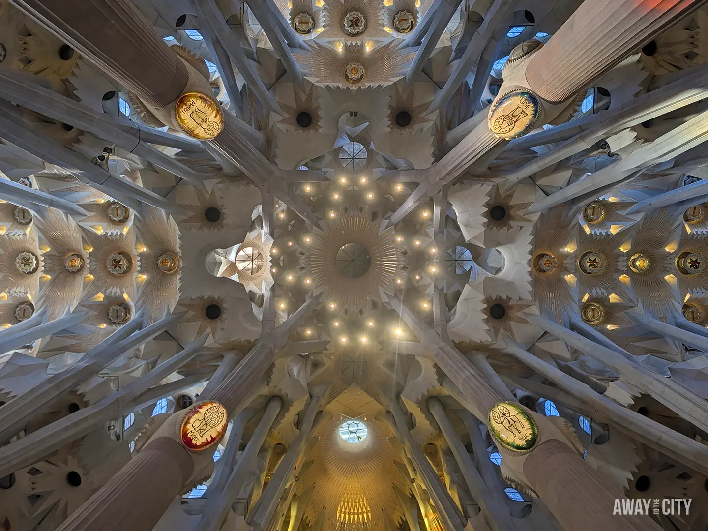 An extreme upward view of the Sagrada Família's ceiling shows the intricate starburst vaults and tree-branch columns.