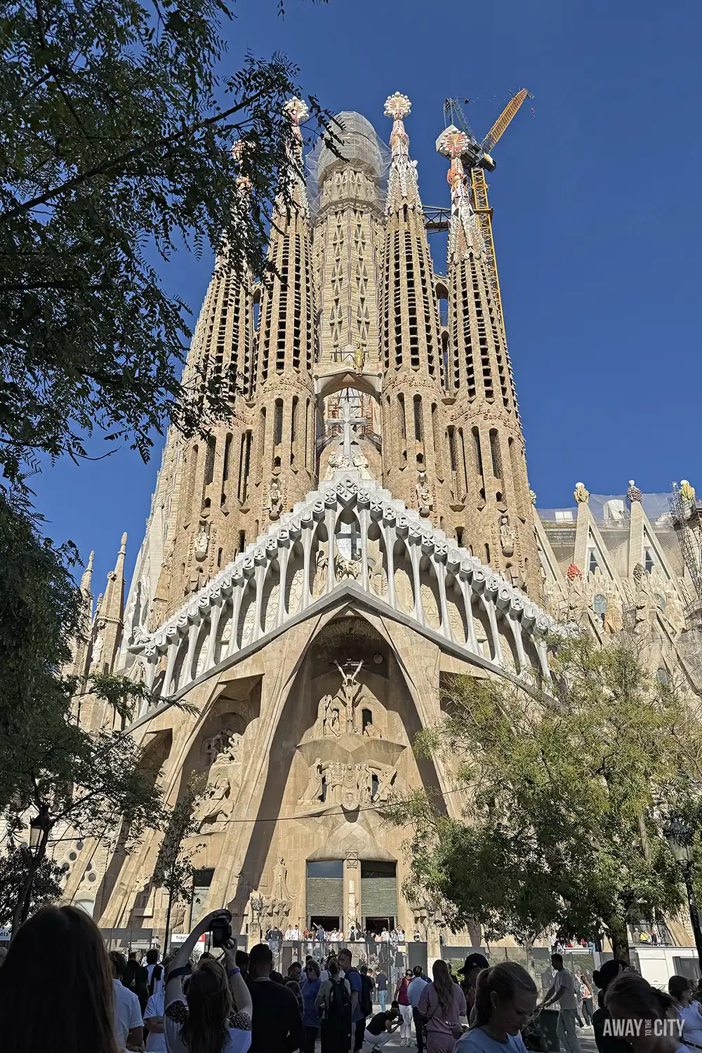 The Sagrada Família's Nativity Façade shows its intricate spires and sculptural detail under construction against a clear blue sky.