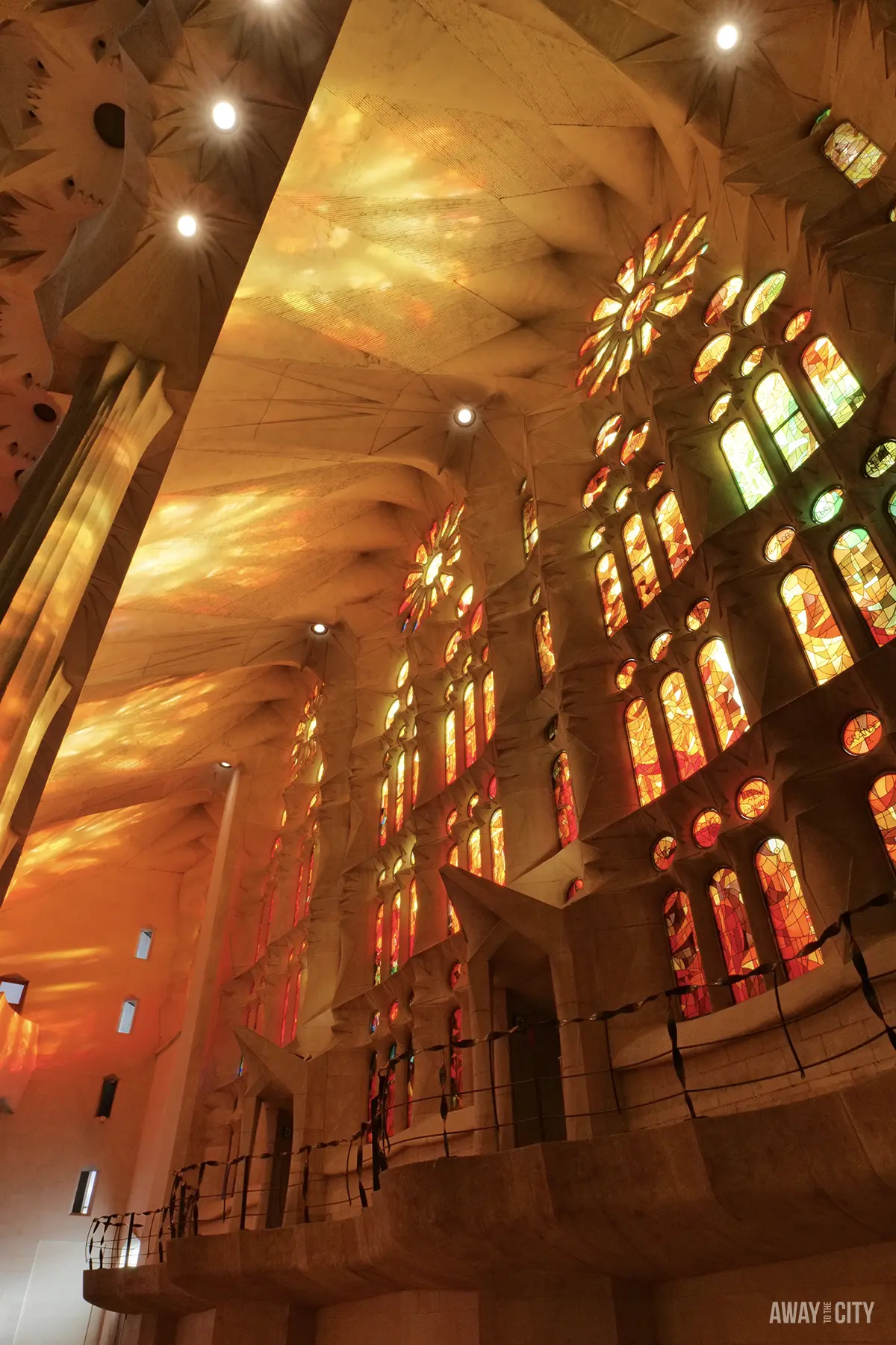 Warm orange light streams through the tall, rectangular stained-glass windows of the Sagrada Família's Passion Façade.