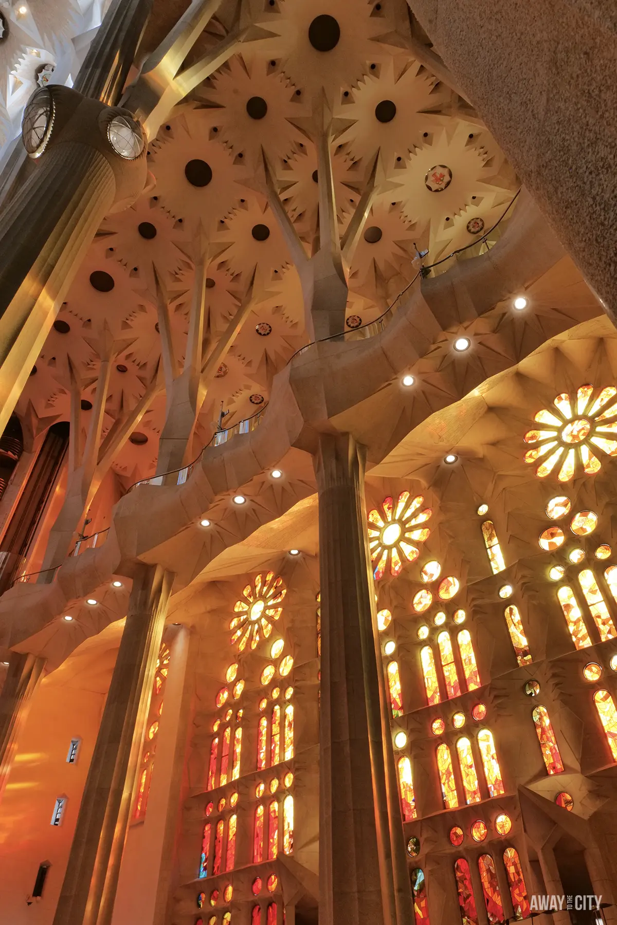 Sunlight dramatically streams through the orange and yellow stained glass windows onto the tree-like columns of the Sagrada Família.