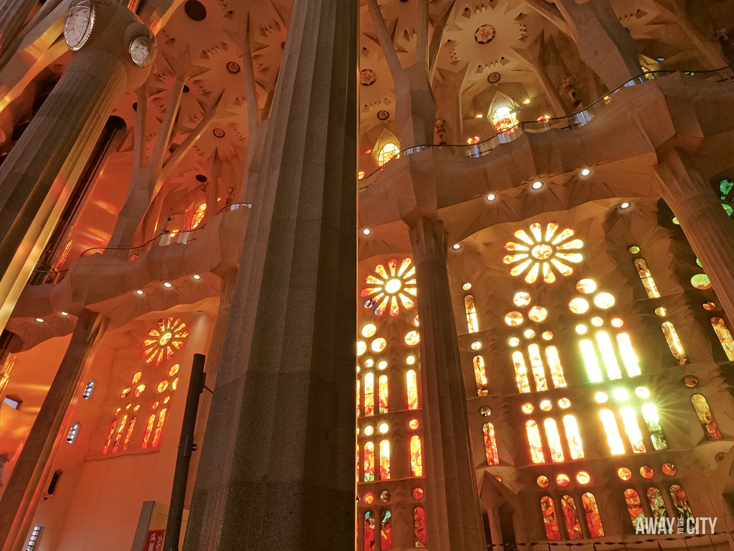 Giant, fluted columns frame the warm, sun-drenched orange and red stained-glass windows of the Sagrada Família.