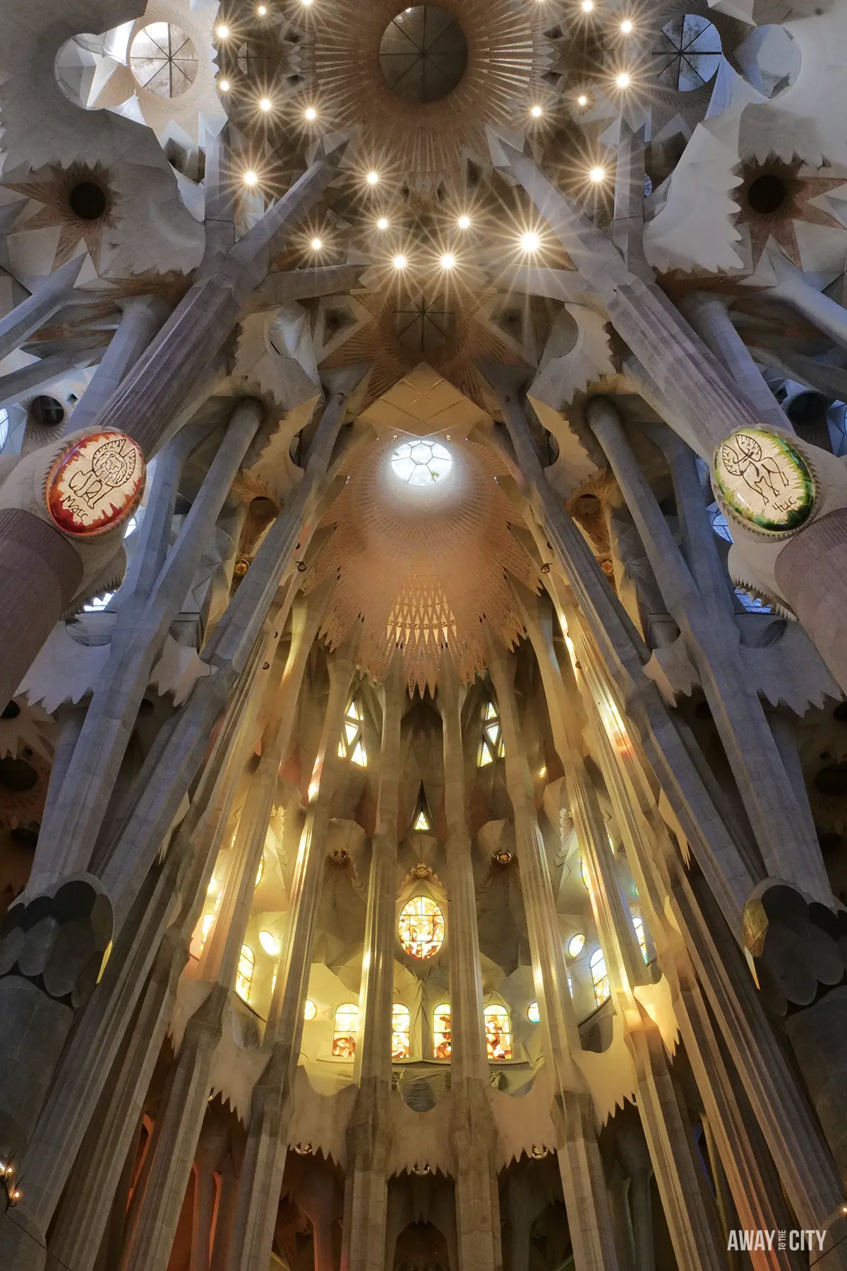 A dramatic upward view shows the tree-like columns soaring to the starburst vaulting of the Sagrada Família's ceiling.
