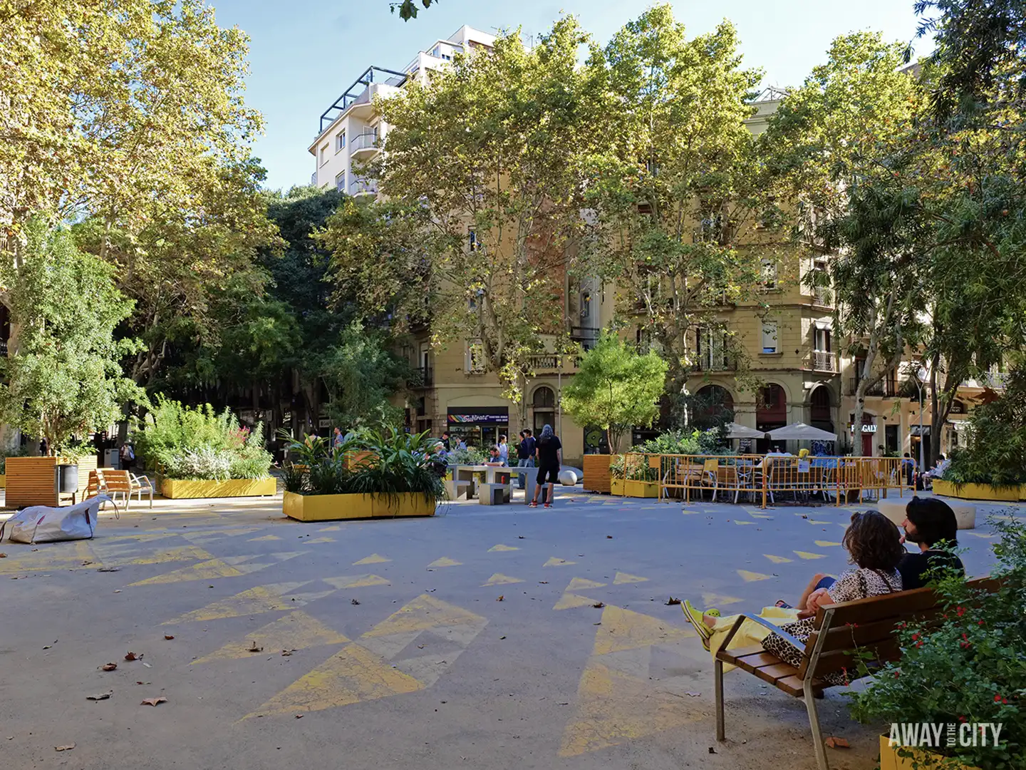 A bright, sunny view of a pedestrianised public square in Barcelona's Sant Antoni Superilla with yellow planters and people relaxing.