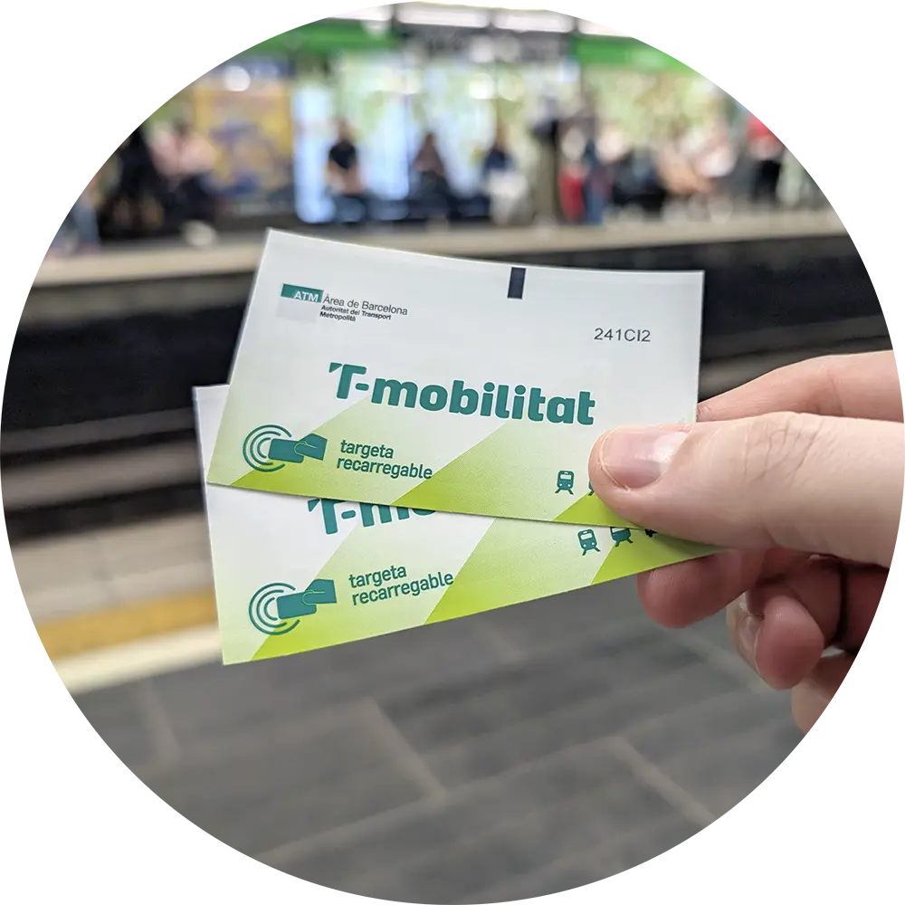 A person with red nail varnish holds two Hola Barcelona Travel Cards for the city's public transport system. A hand holds two green and white T-mobilitat rechargeable cards for Barcelona's integrated public transport system.