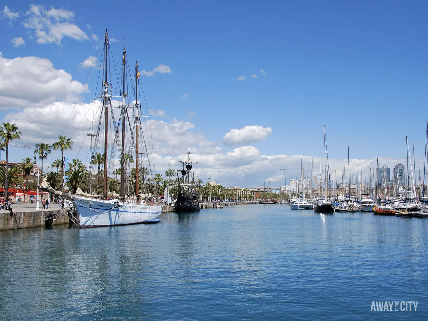 A bright, sunny view of Barcelona's Port Vell with a large tall ship docked beside a marina full of sailboats.