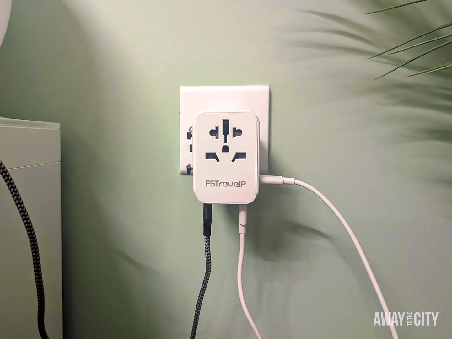 Universal travel adaptor plugged into a wall socket with two charging cables connected, demonstrating a practical travel packing essential.